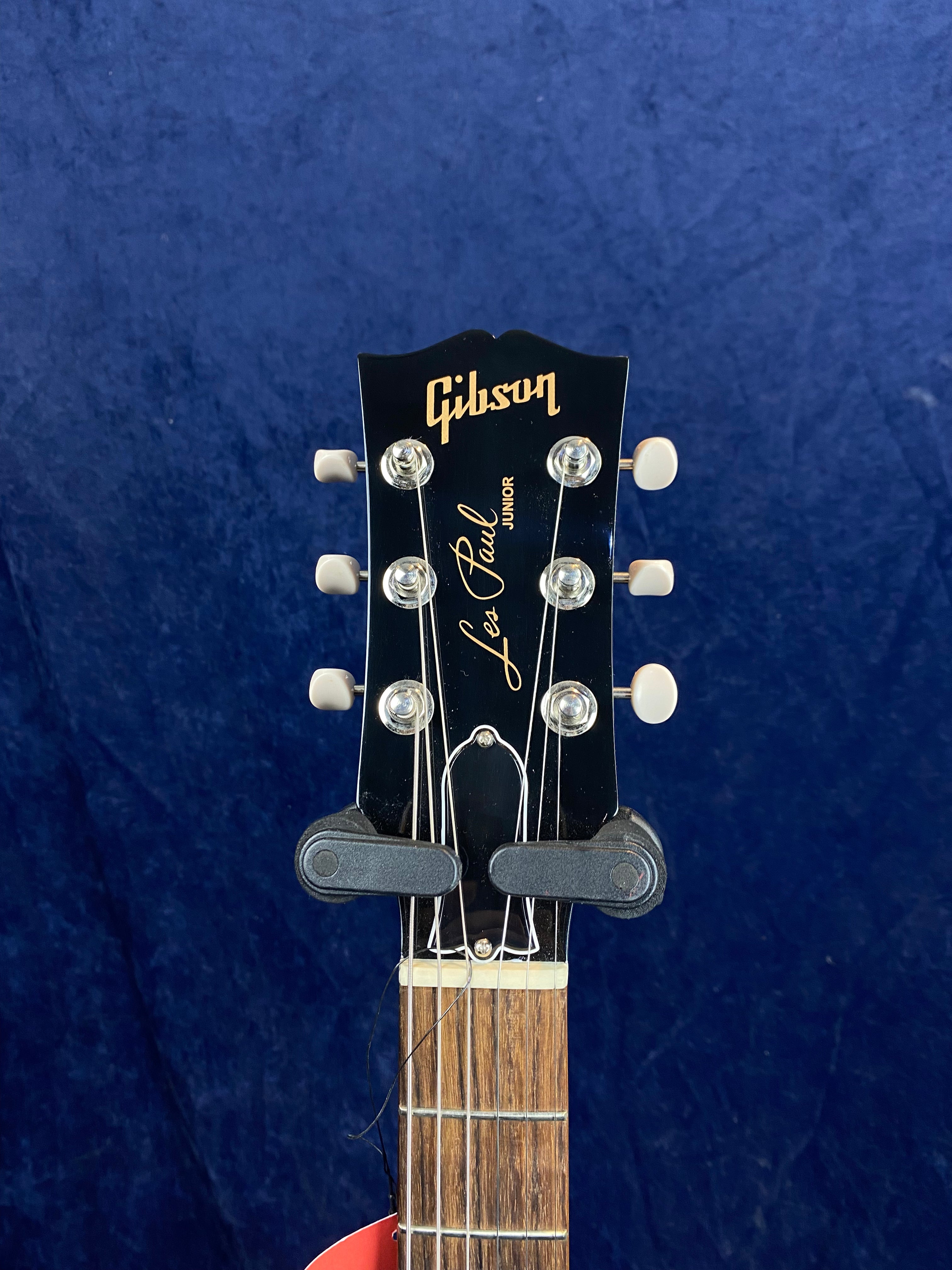 Gibson Les Paul Junior electric guitar headstock with six tuning pegs, truss rod cover, and gold Gibson logo on a dark background.