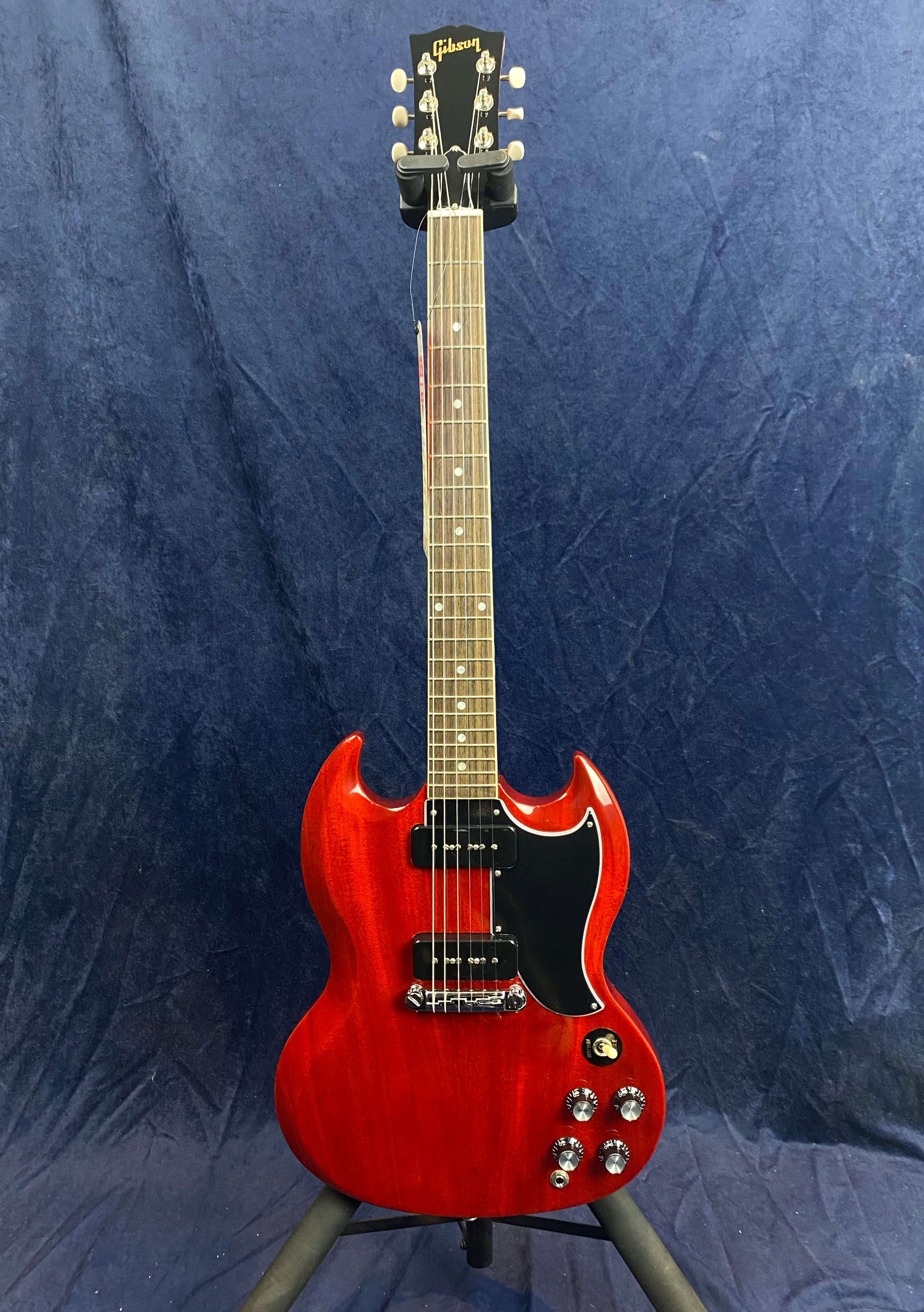 Red Gibson electric guitar with double-cutaway body, two black pickups, four control knobs, and a black pickguard, standing on a tripod stand.