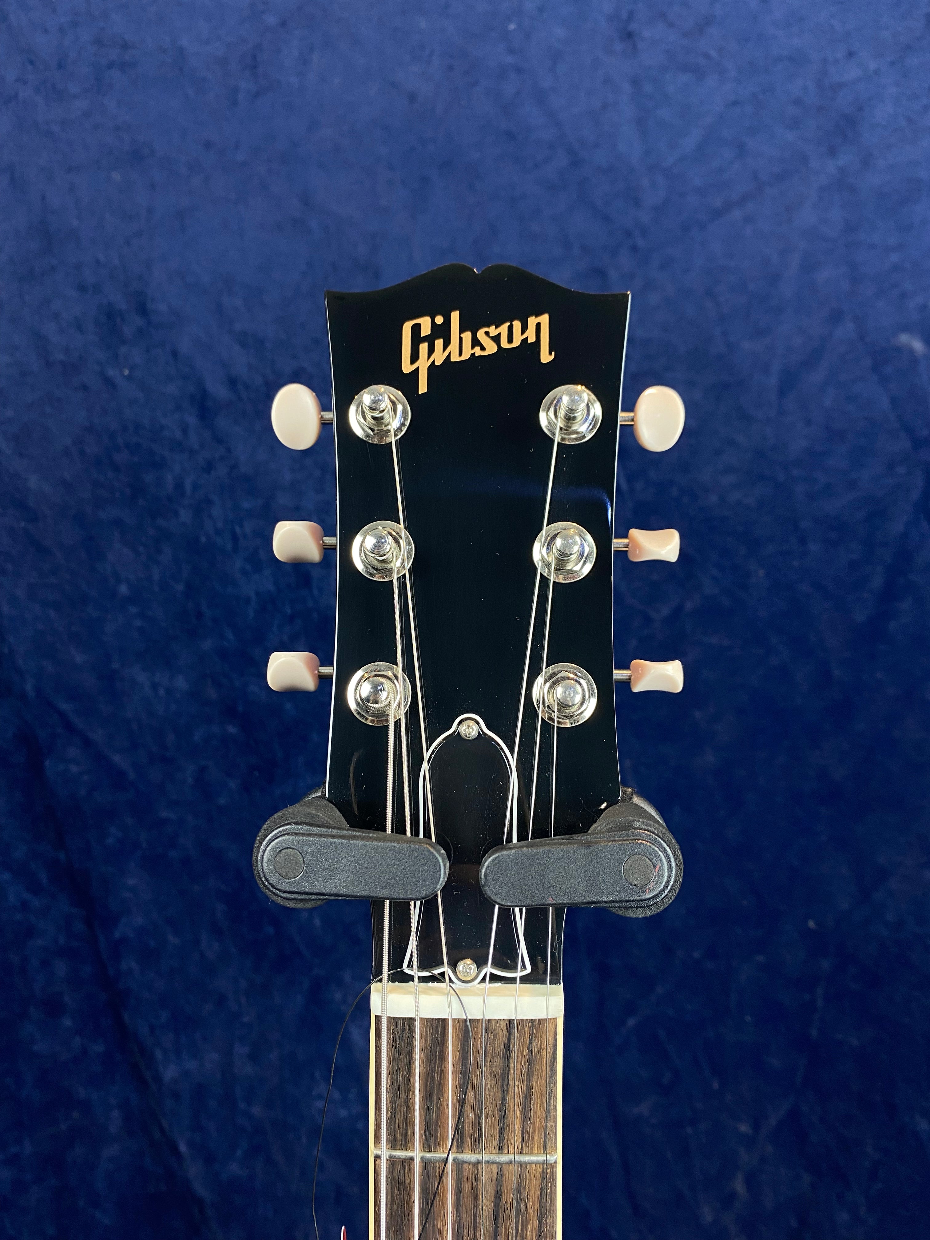 Headstock of a Gibson electric guitar with six tuning pegs, gold Gibson logo, and a capo attached just above the nut.