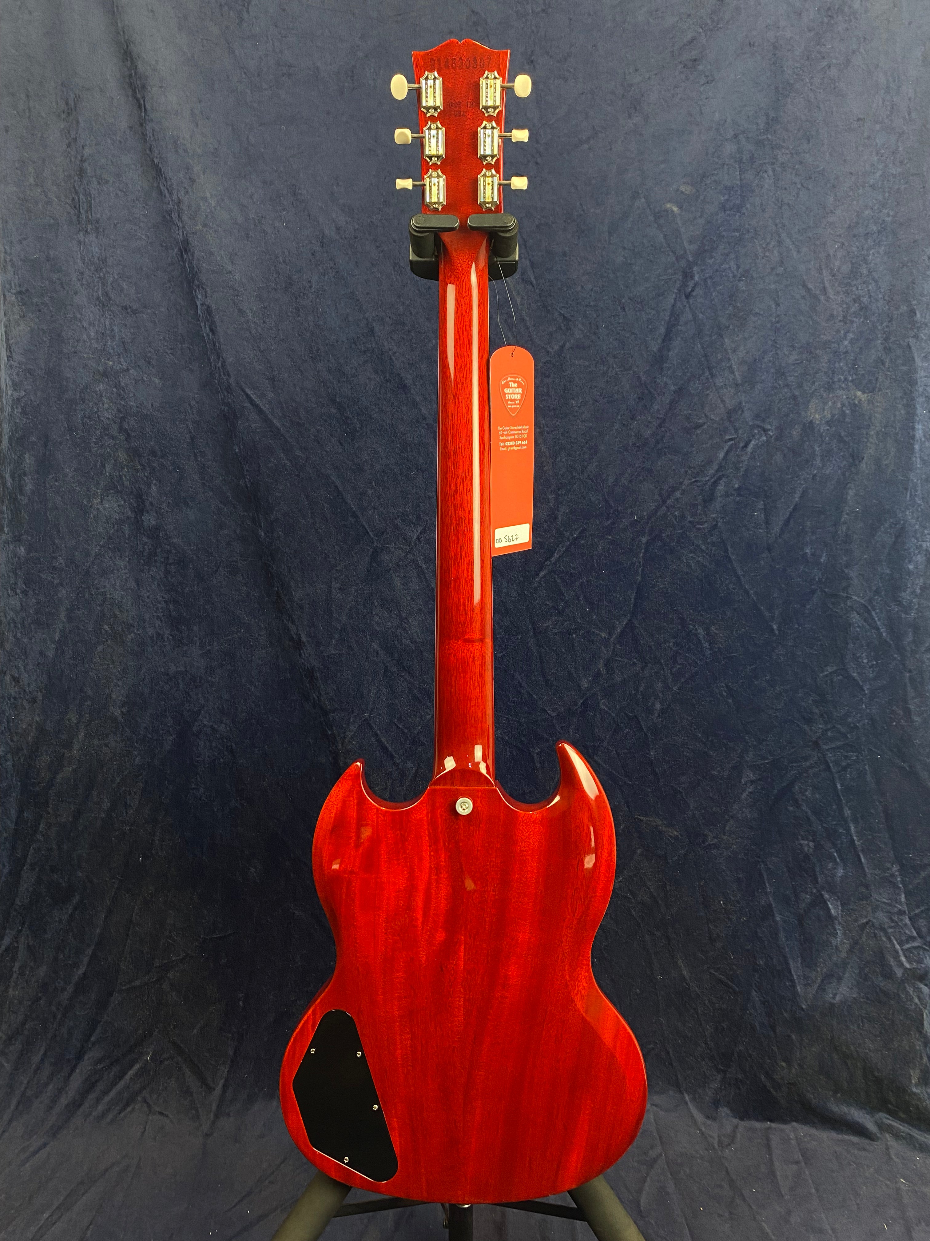 Cherry red electric guitar seen from the back, showing a glossy finish, double cutaway body, and six tuning pegs on the headstock.