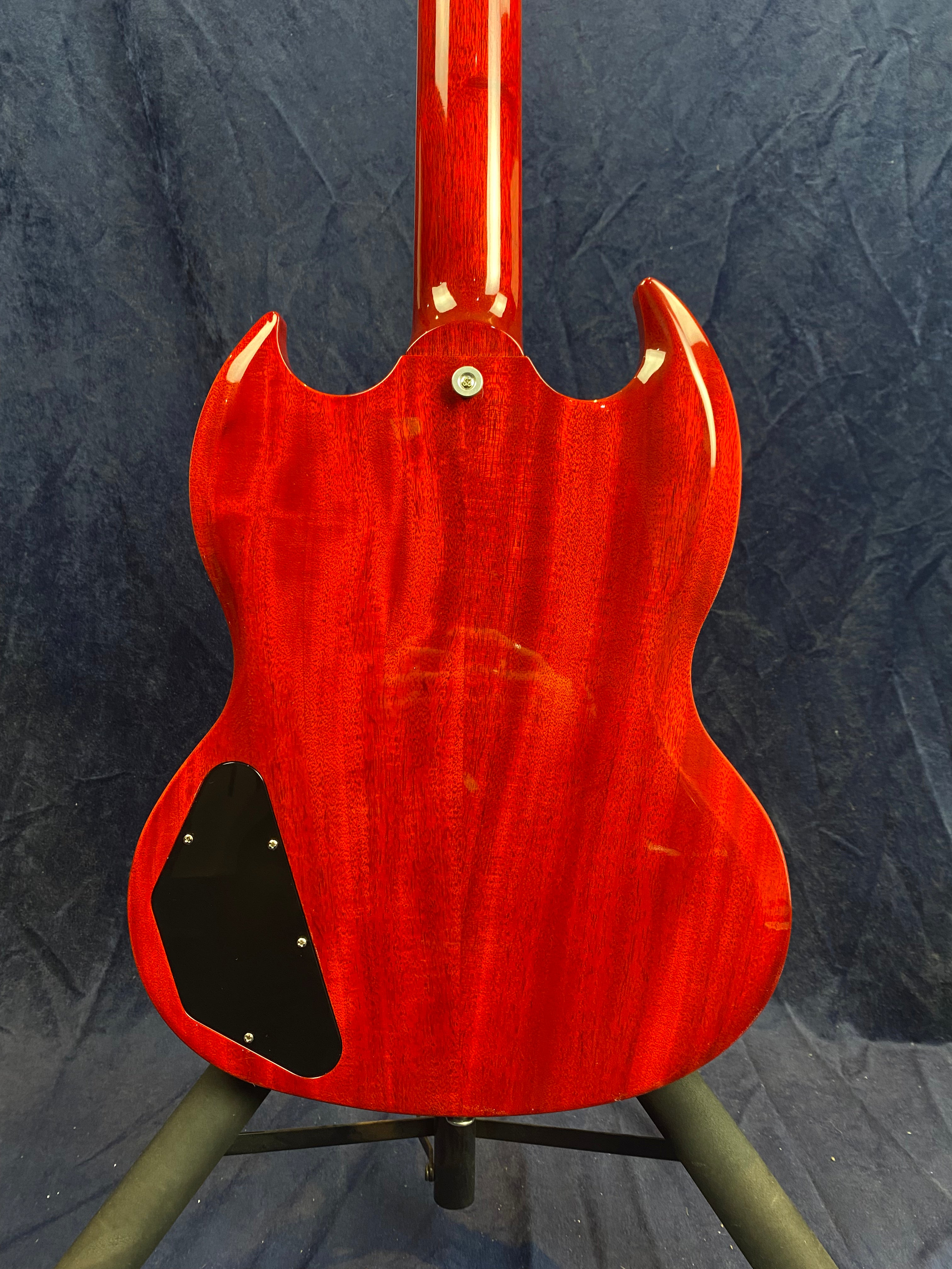 Back of a red electric guitar with a glossy finish, black electronics cover on the lower left, and dual cutaway body shape.