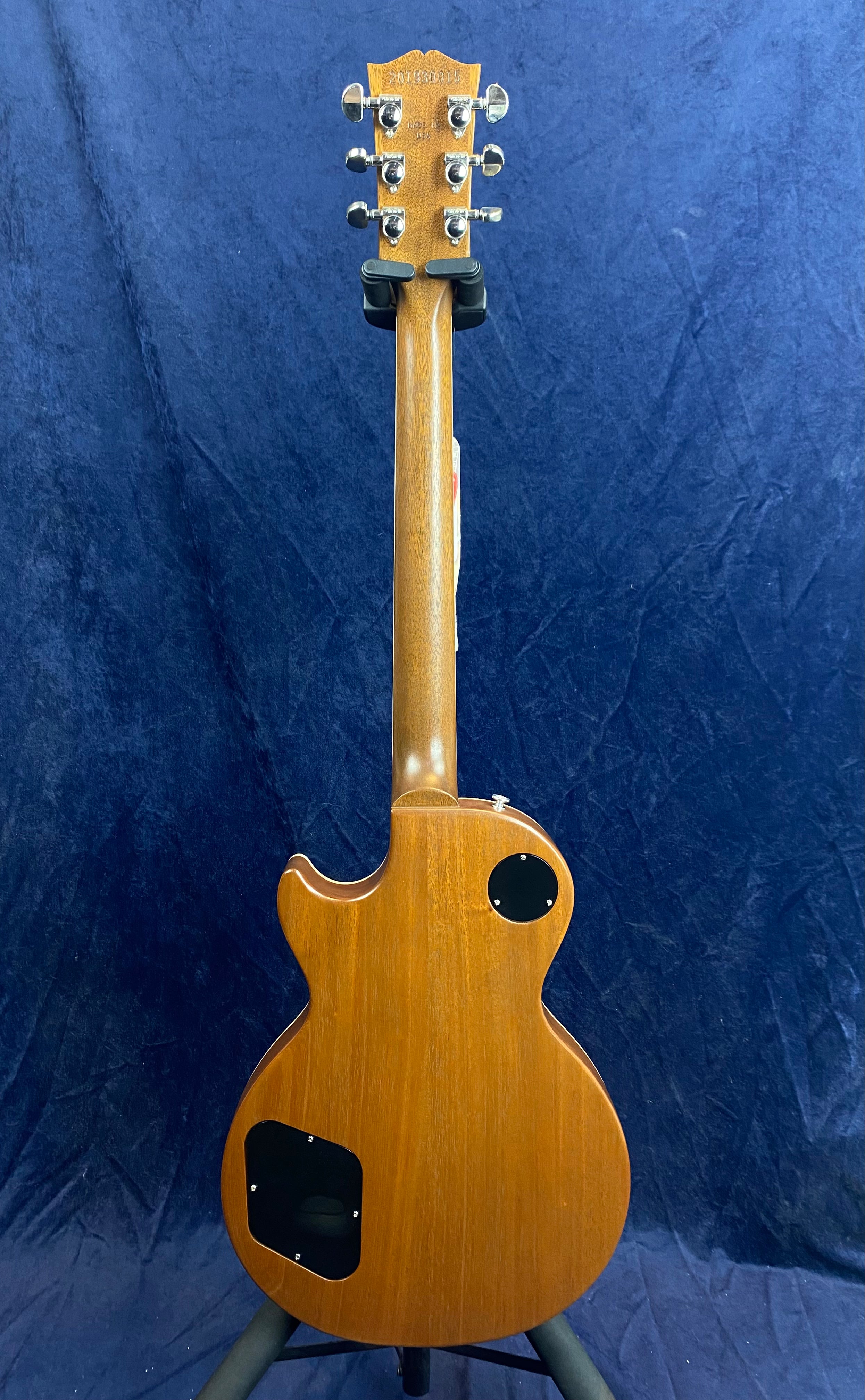 Electric guitar with a natural wood finish shown from the back, featuring chrome tuners and two black plastic access covers on the body.
