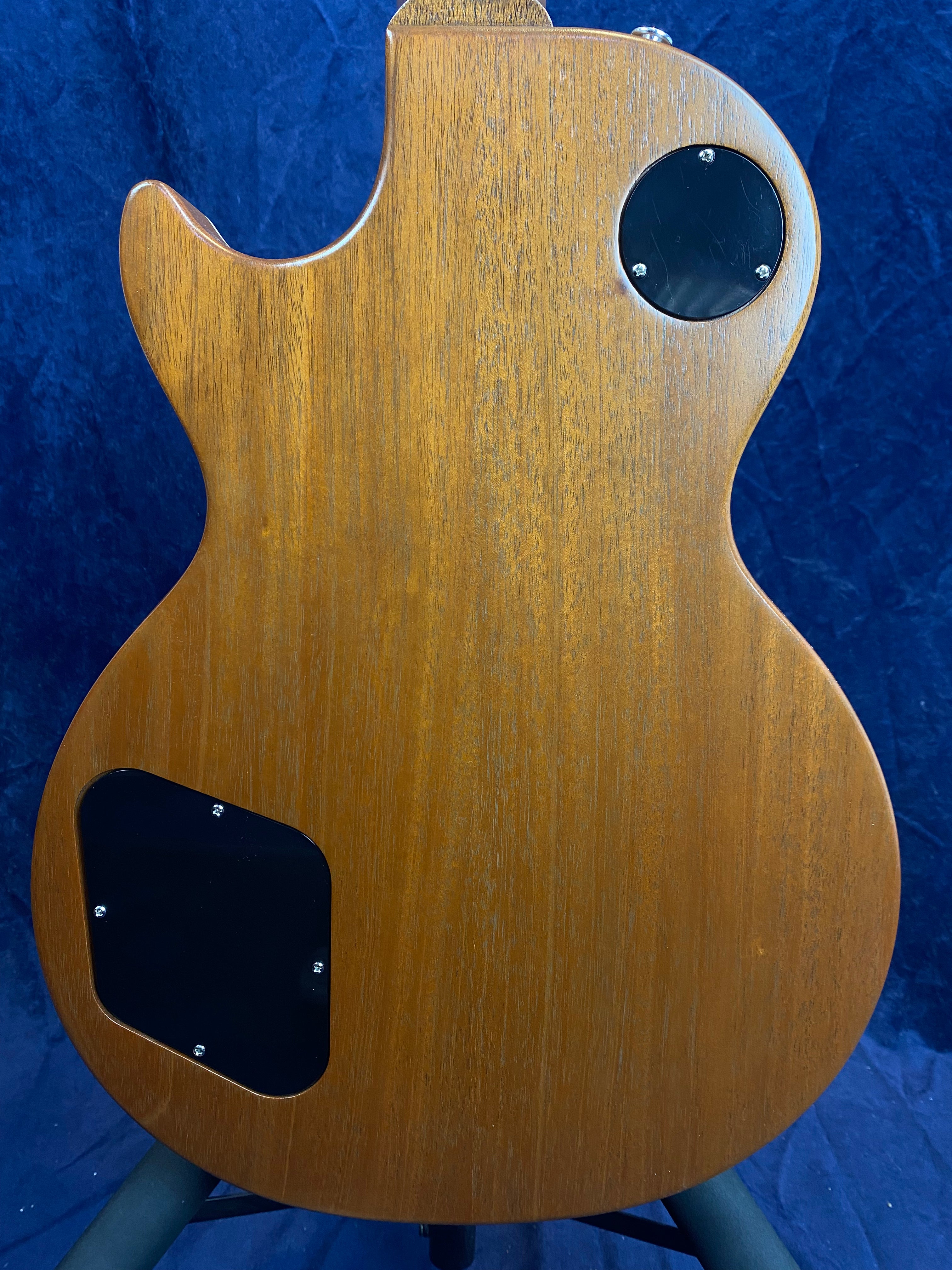 Natural wood-finish electric guitar back with two black plastic control cavity covers, one round near the neck and one rectangular near the bottom.