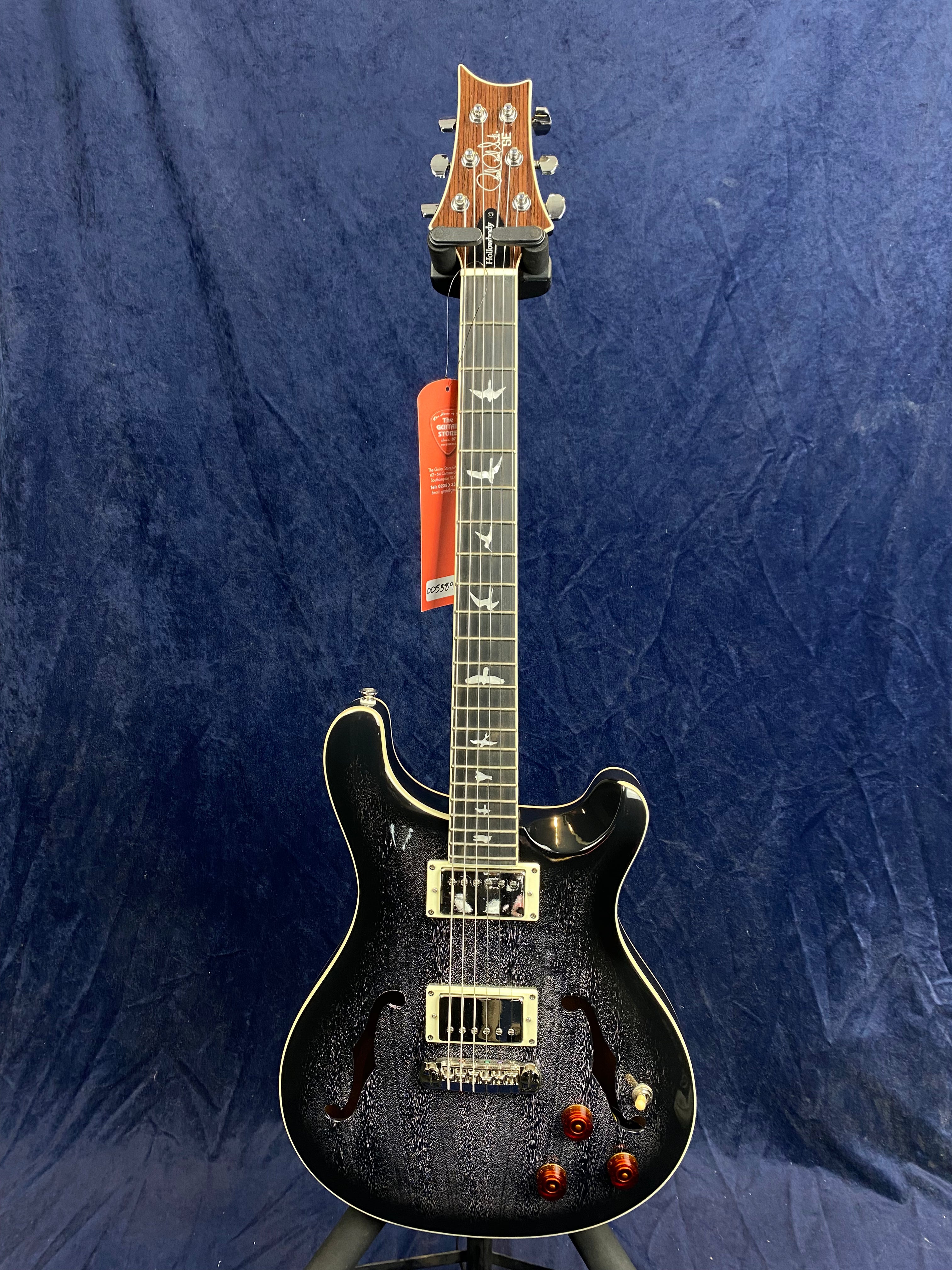 Glossy black electric guitar with two f-holes, dual pickups, bird inlays on the fretboard, wooden headstock, and four amber control knobs.