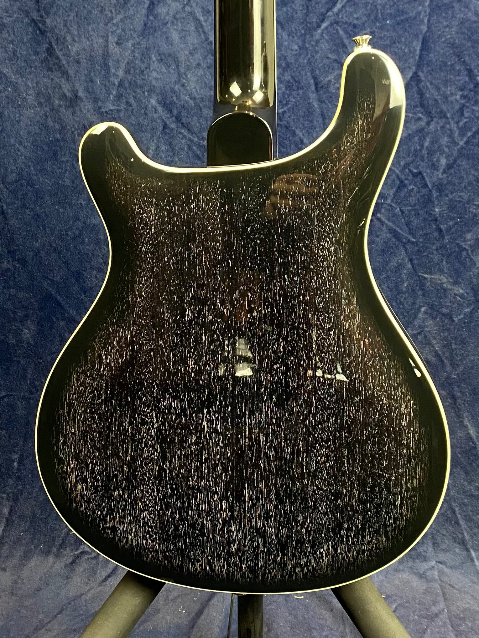 Black electric guitar with a glossy finish, white binding on the edge, and a textured, speckled wood grain pattern on the back against a dark background.