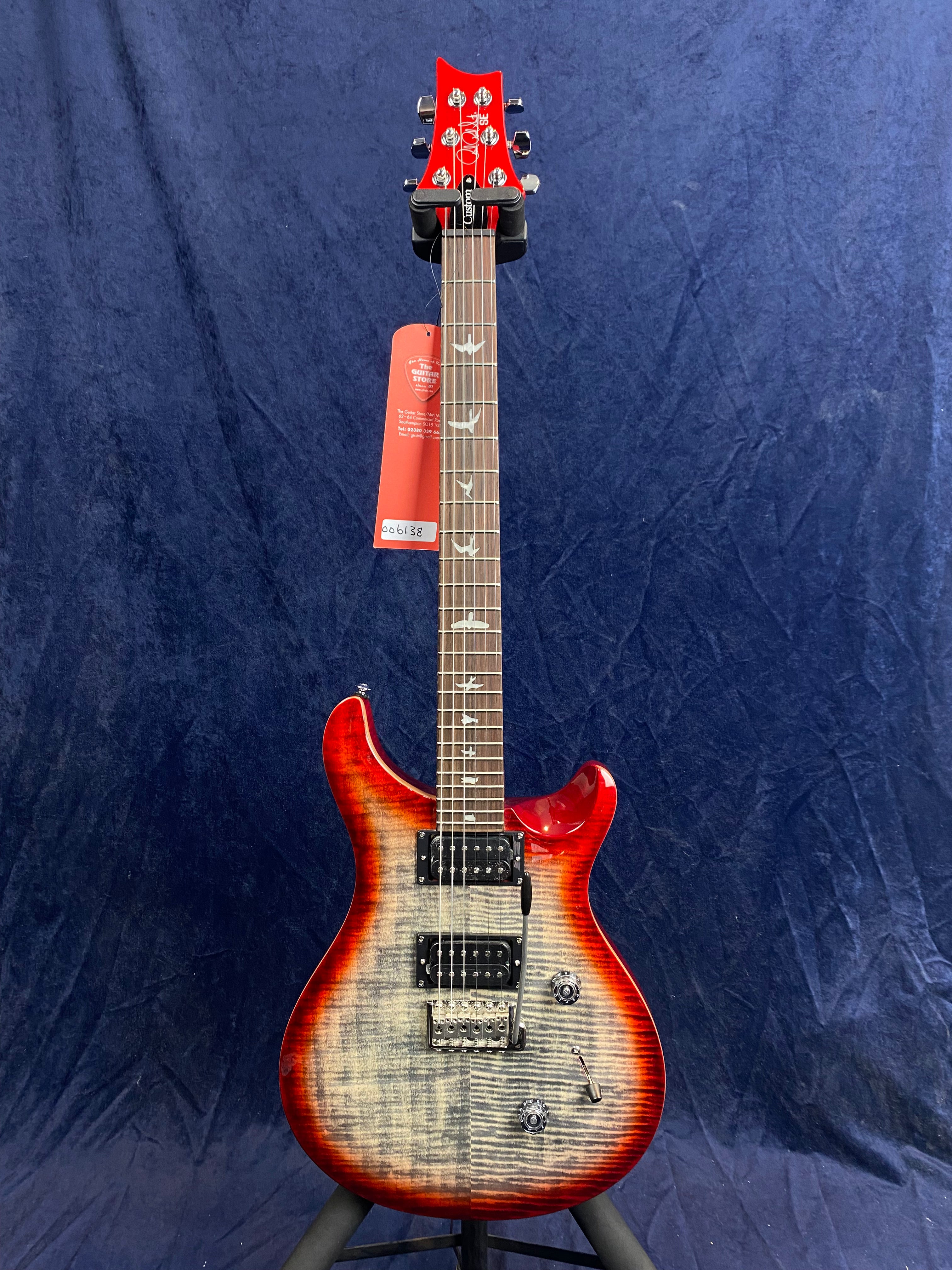 Electric guitar with a glossy red burst finish, two humbucker pickups, bird inlays on the fretboard, and a whammy bar, shown upright against a dark background.