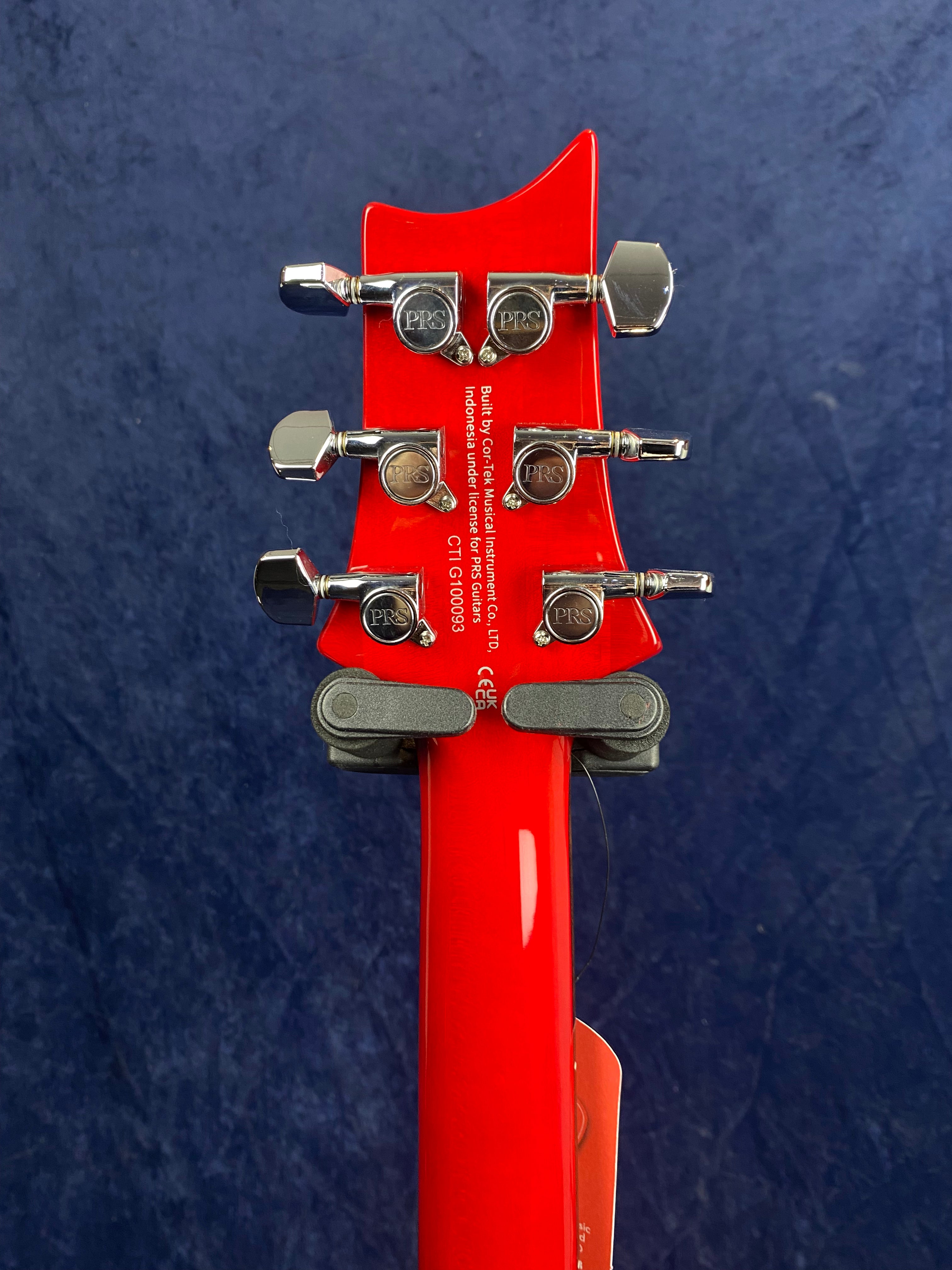 Red electric guitar headstock with six chrome PRS tuning pegs and manufacturer information printed in white on the back.