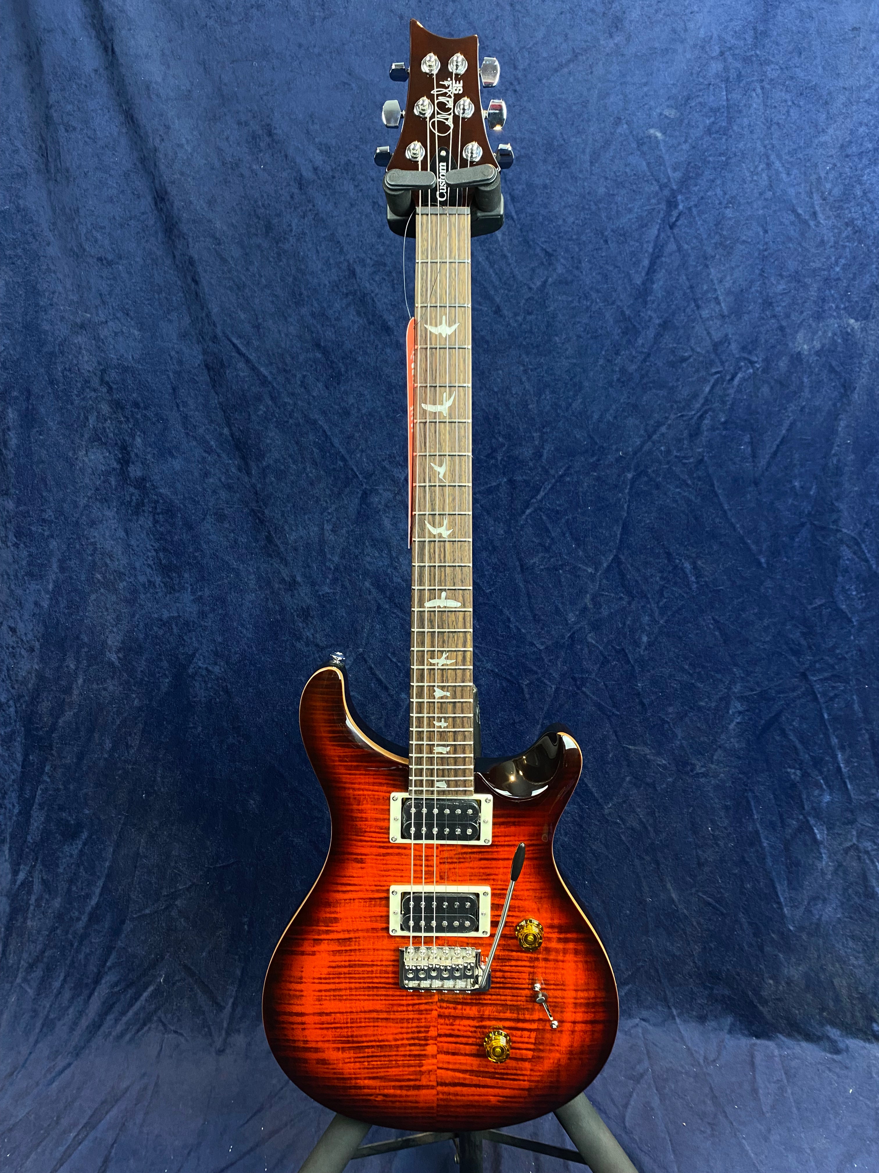 Electric guitar with a glossy red sunburst finish, dual humbucker pickups, bird inlays on the fretboard, and two amber control knobs.
