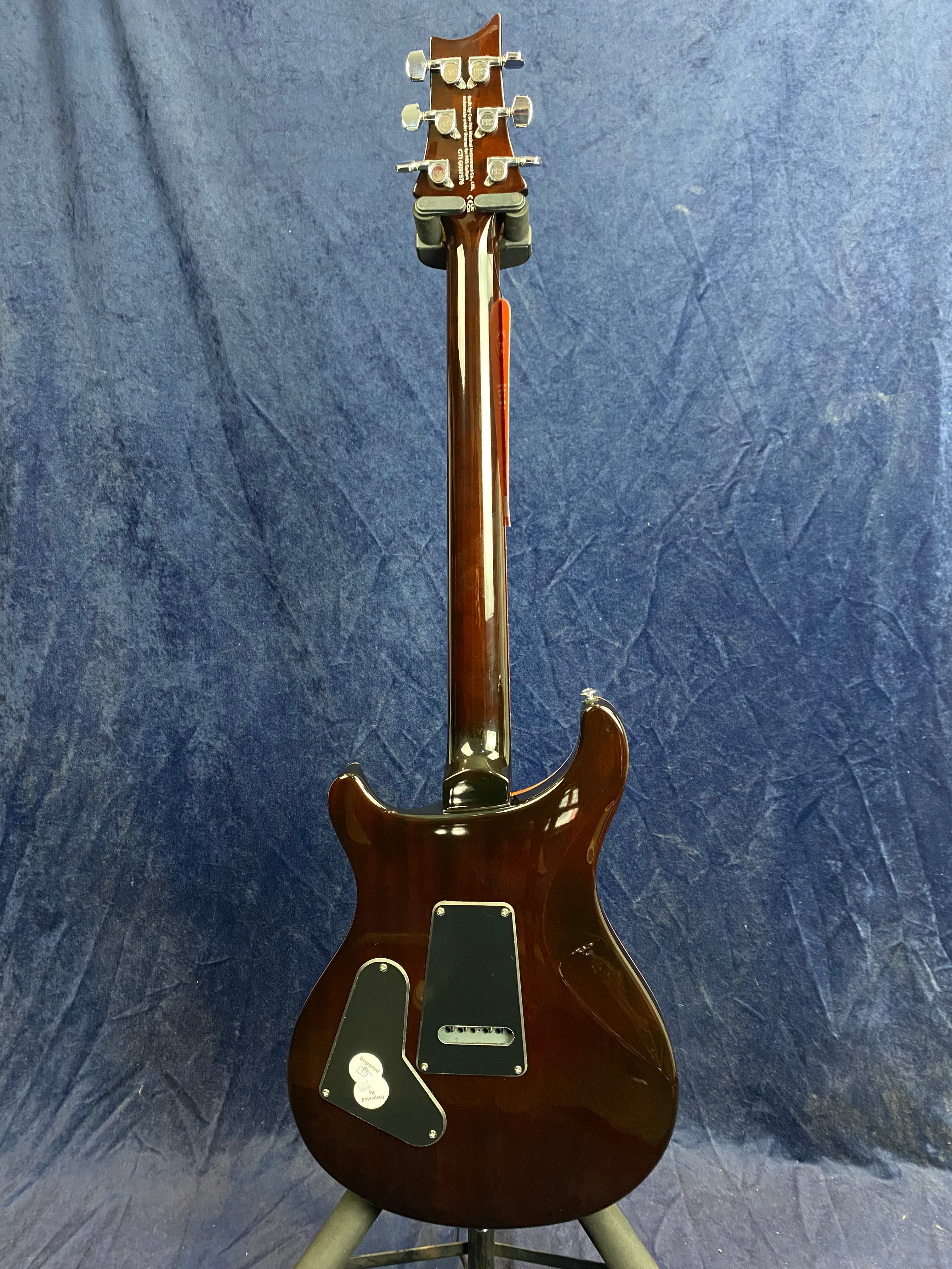 Glossy brown electric guitar shown from the back, highlighting two black control cavity covers and chrome tuning pegs on the headstock.