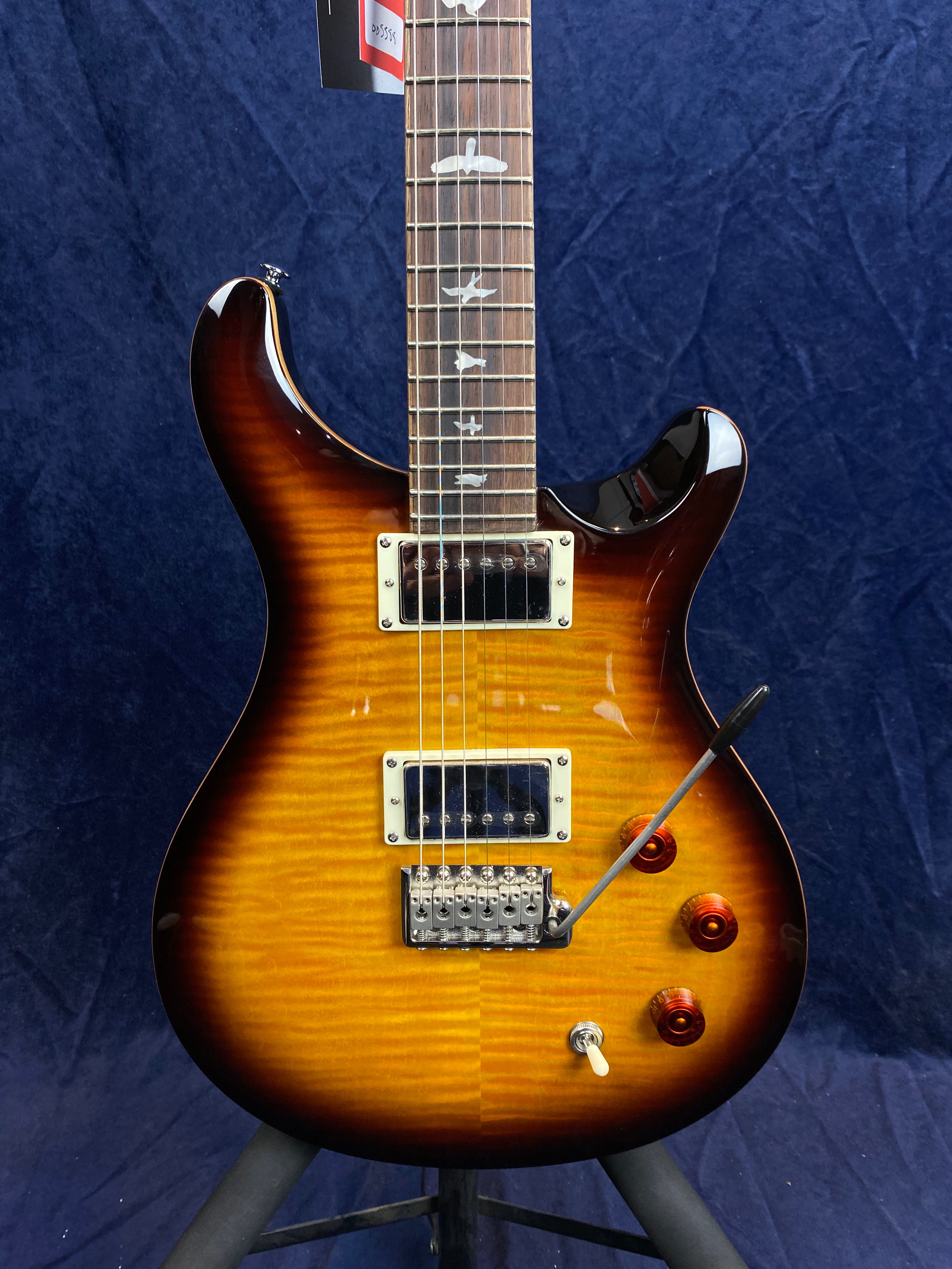 Sunburst electric guitar with two humbucker pickups, three amber control knobs, a tremolo bar, and bird-shaped inlays on the fretboard.