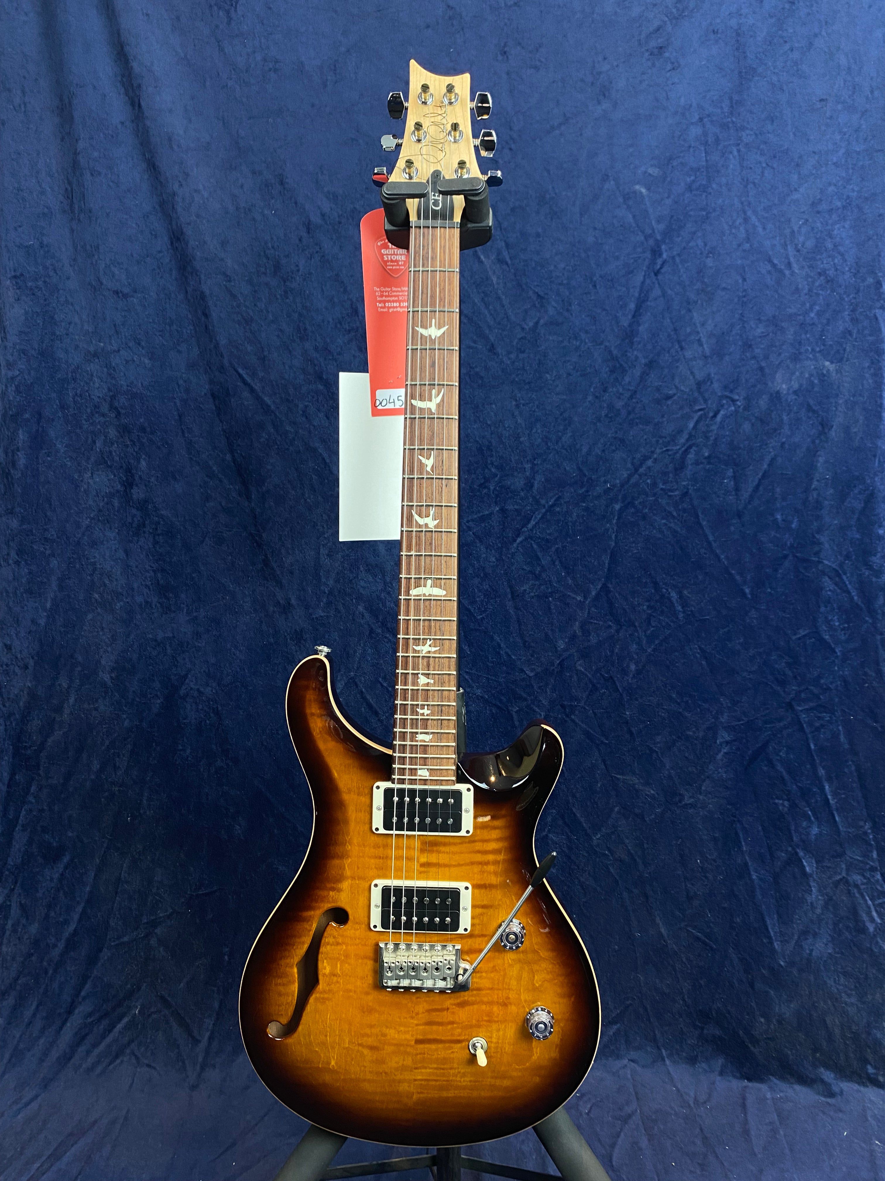 Sunburst electric guitar with a semi-hollow body, two humbucker pickups, bird inlays on the fretboard, and chrome hardware against a blue background.