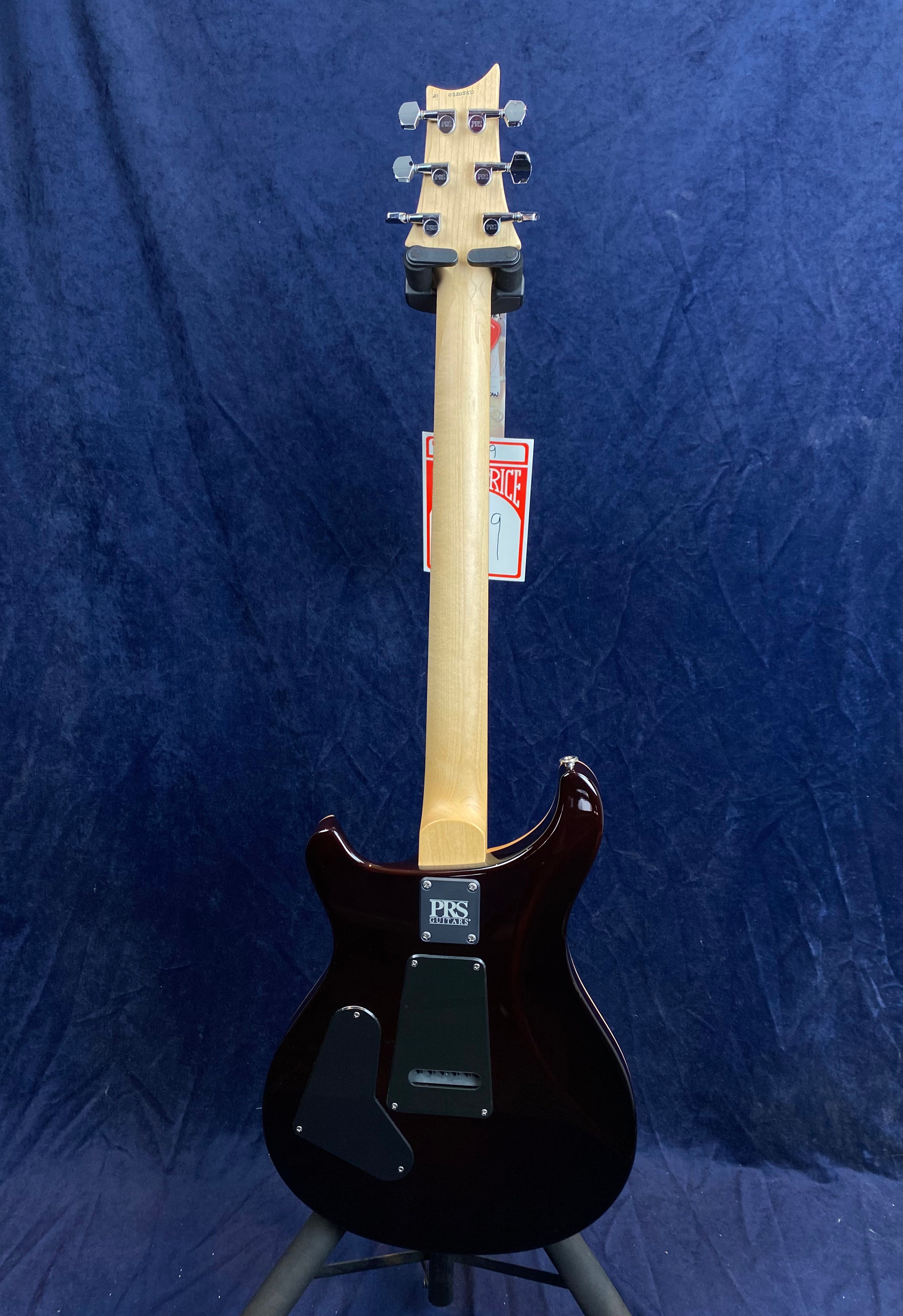 Rear view of a PRS electric guitar with a natural wood neck, dark glossy body, and chrome tuning pegs, displayed on a stand.