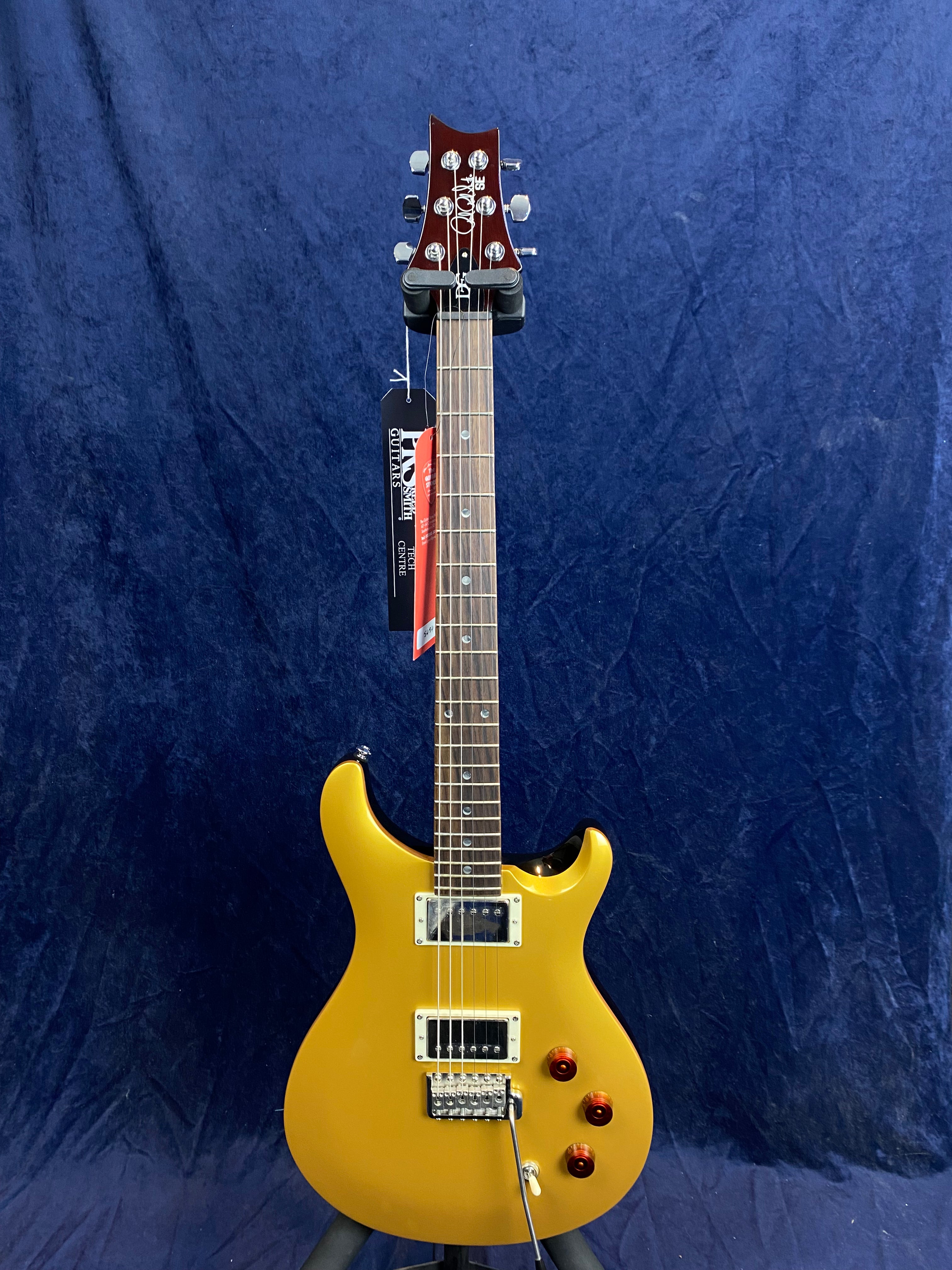 Gold electric guitar with two humbucker pickups, three amber knobs, a tremolo bridge, and a rosewood fretboard against a dark blue background.