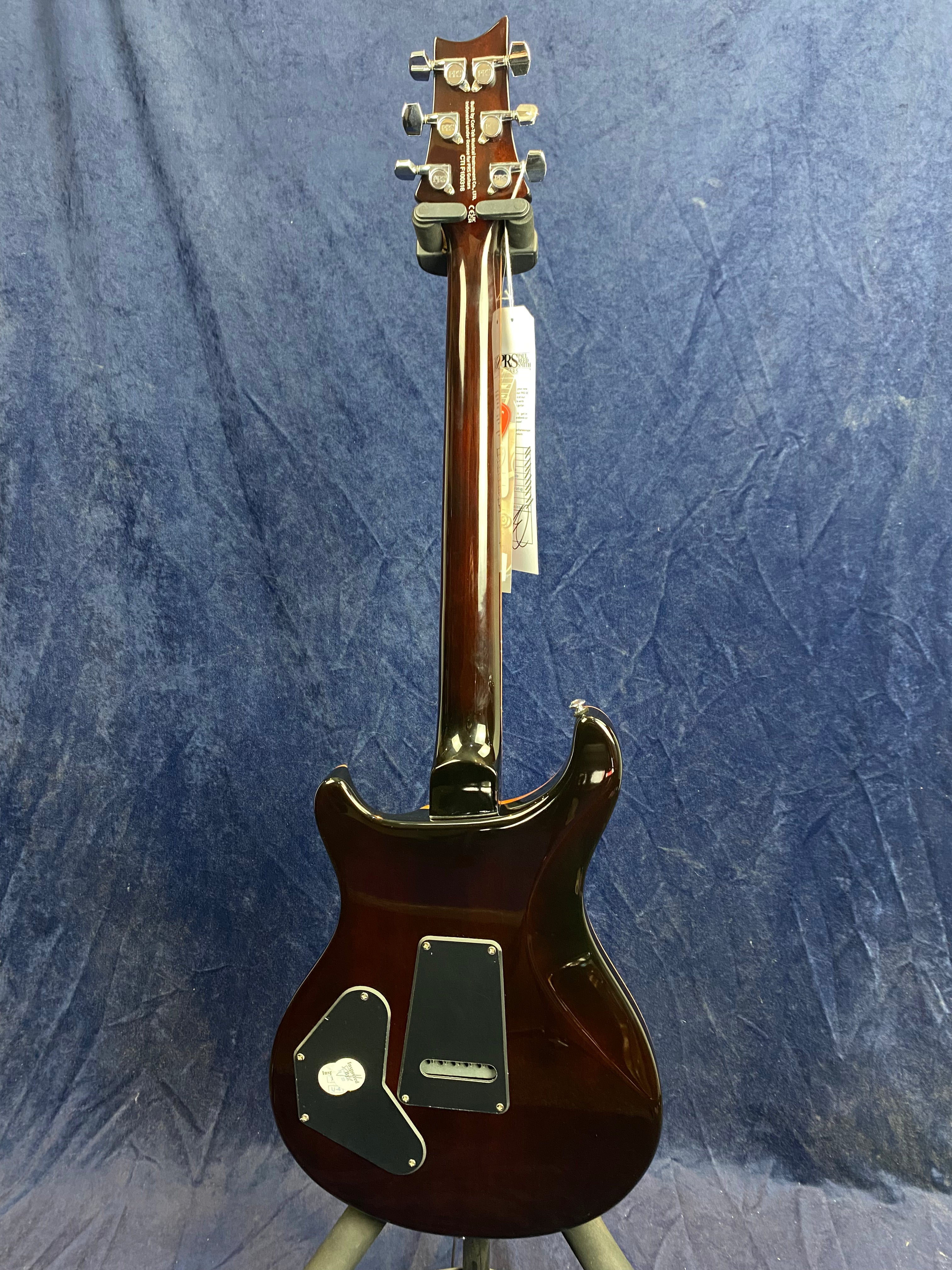 Mahogany-finished electric guitar shown from the back, featuring chrome tuners, two black plastic cavity covers, and a tag hanging from the headstock.
