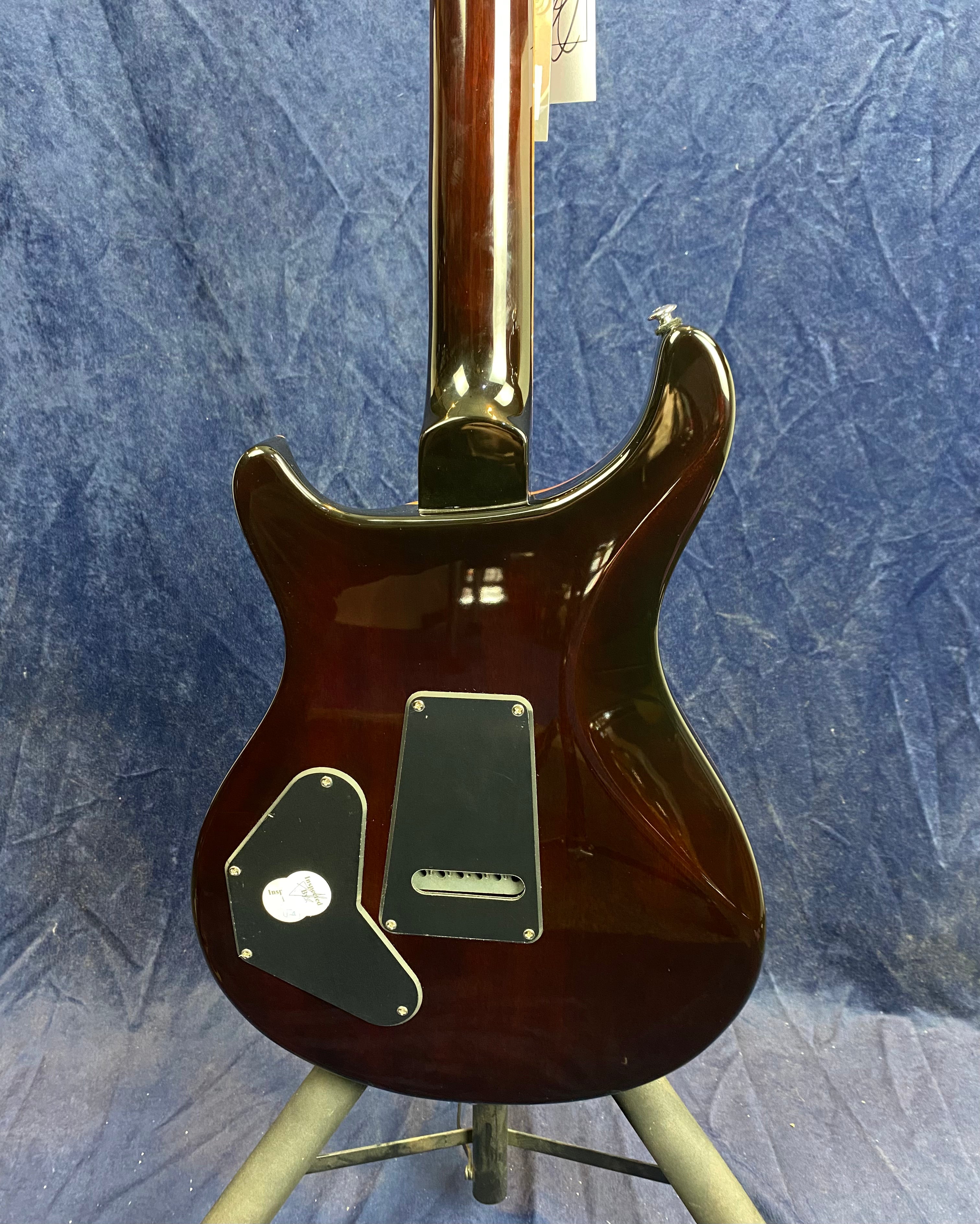 Back view of a dark, glossy electric guitar body with two black plastic electronics covers and a strap button on the upper horn.