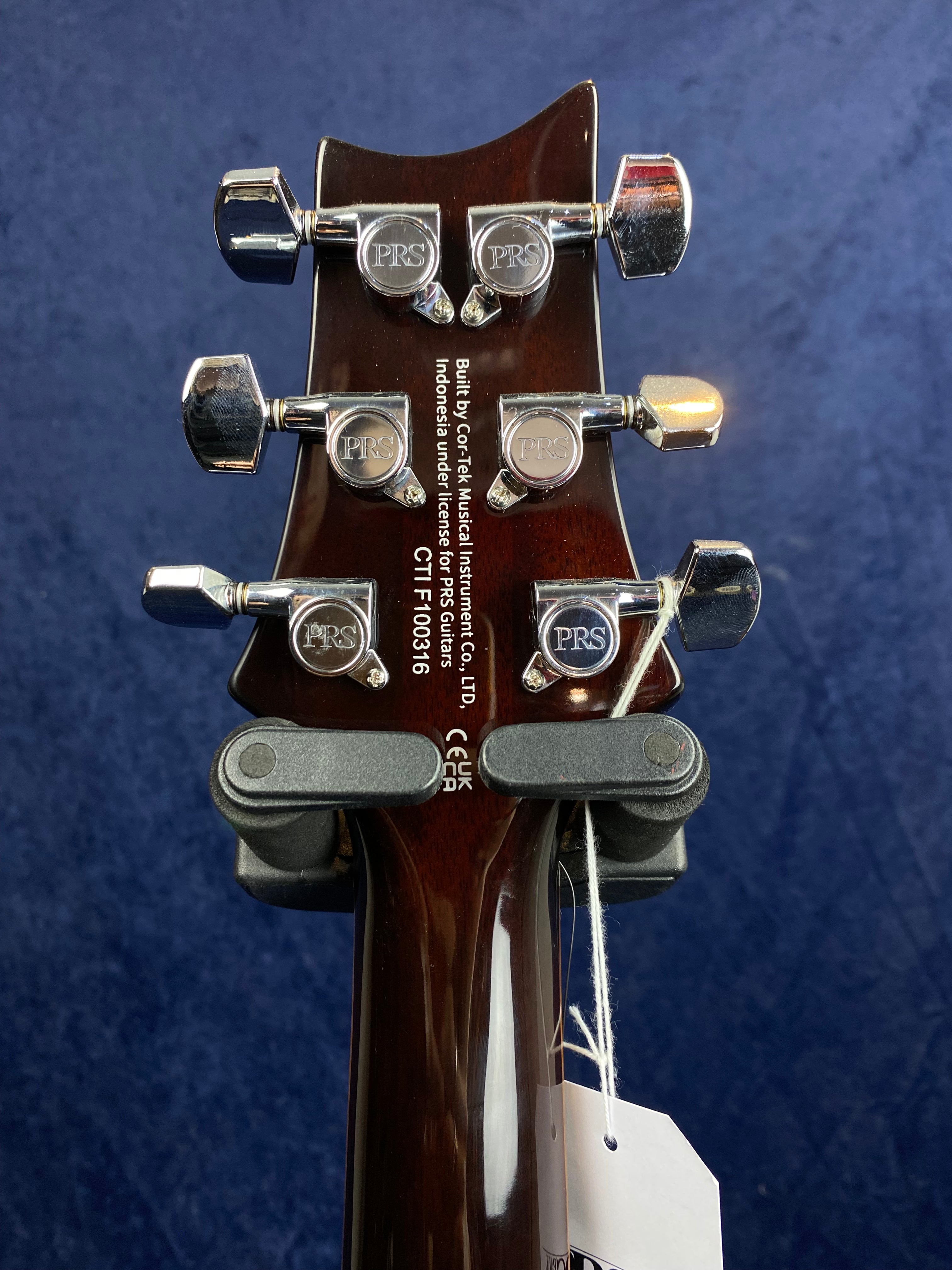 Six chrome tuning pegs marked "PRS" line the dark wood headstock of a PRS electric guitar, with manufacturer info and serial number in white text.