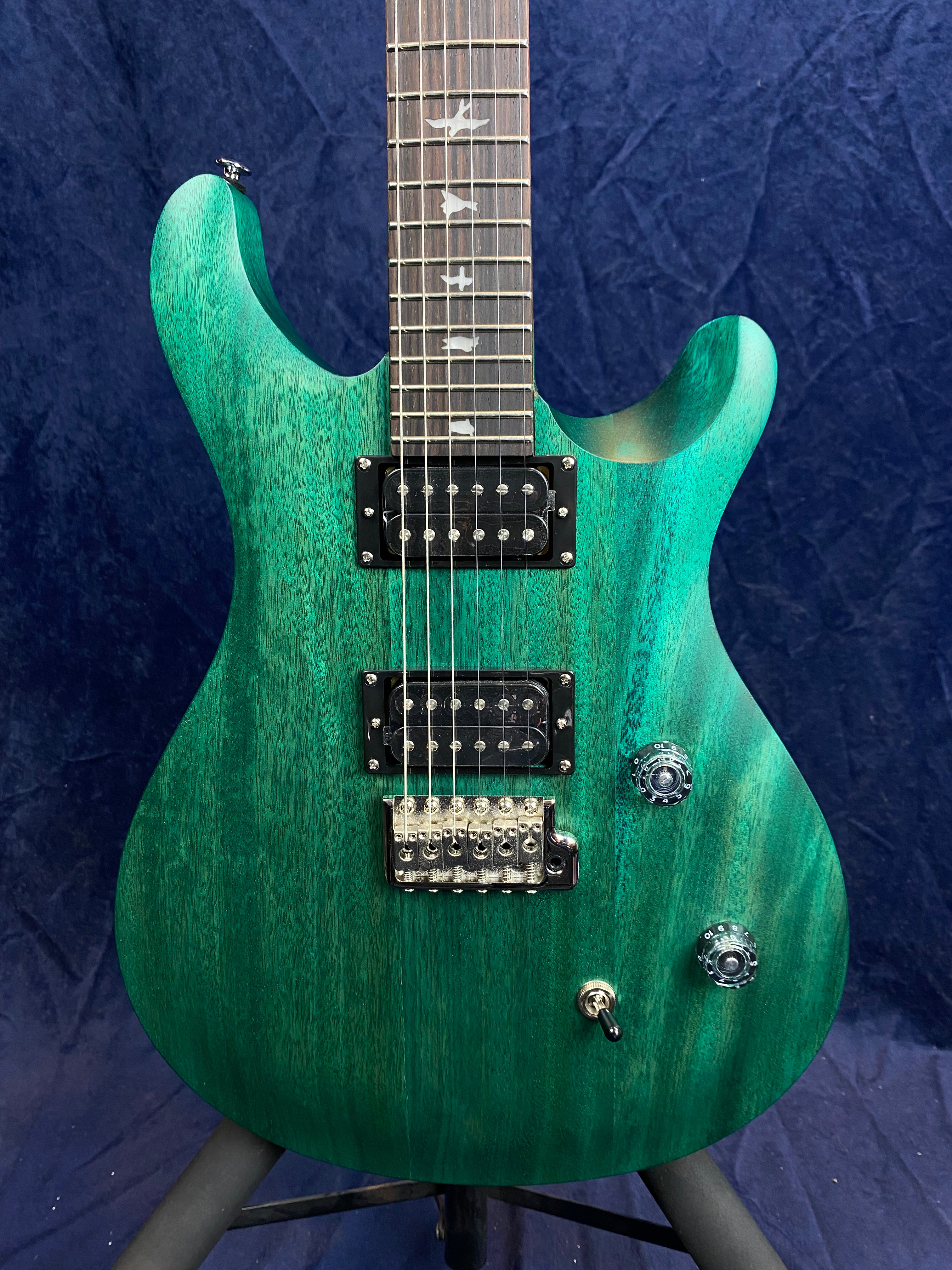 Teal green electric guitar with dual humbucker pickups, three control knobs, a switch, and bird inlays on a rosewood fingerboard.