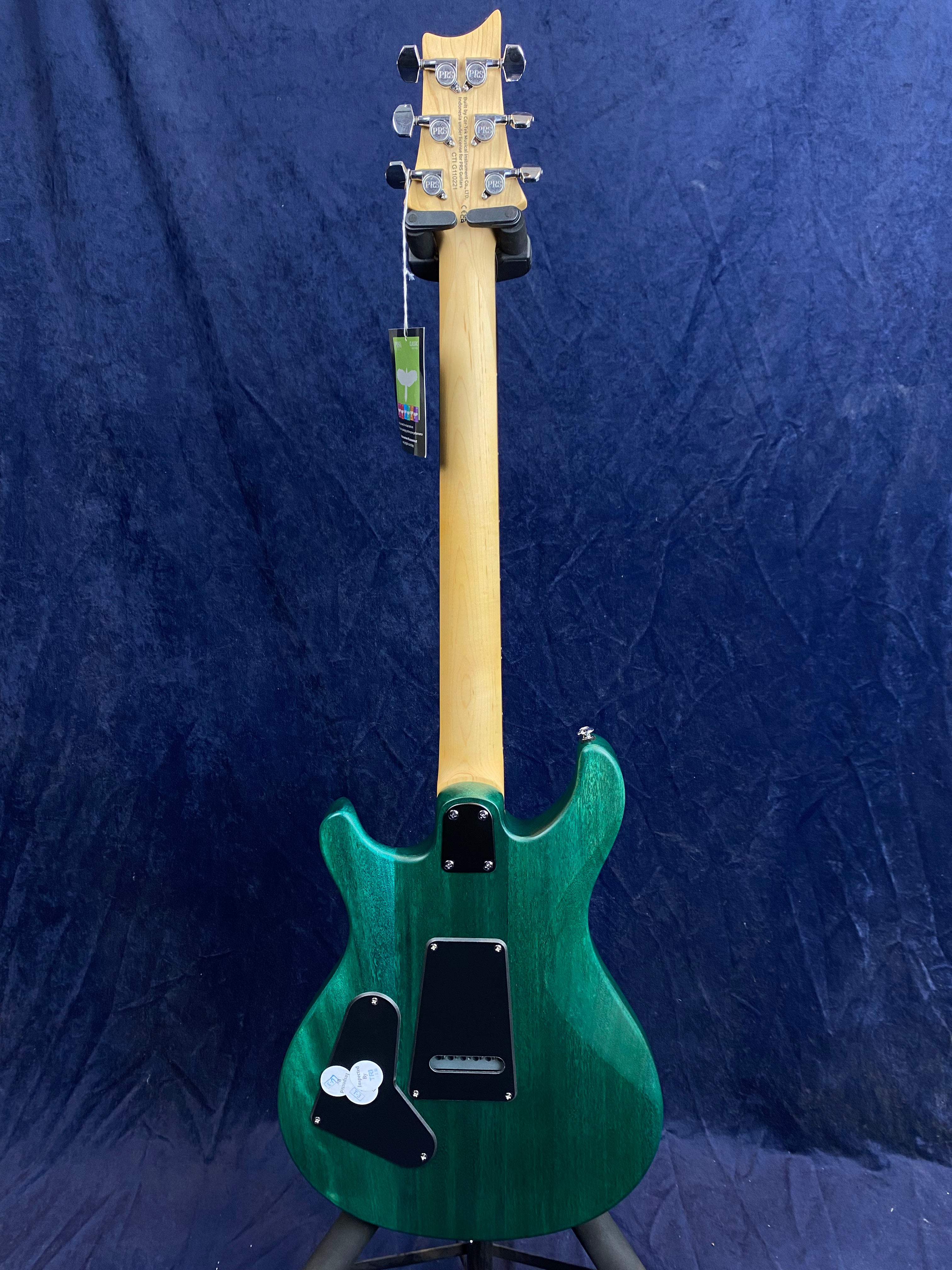 Green electric guitar shown from the back, revealing wood grain, three black plastic covers, natural wood neck, and chrome tuning pegs.