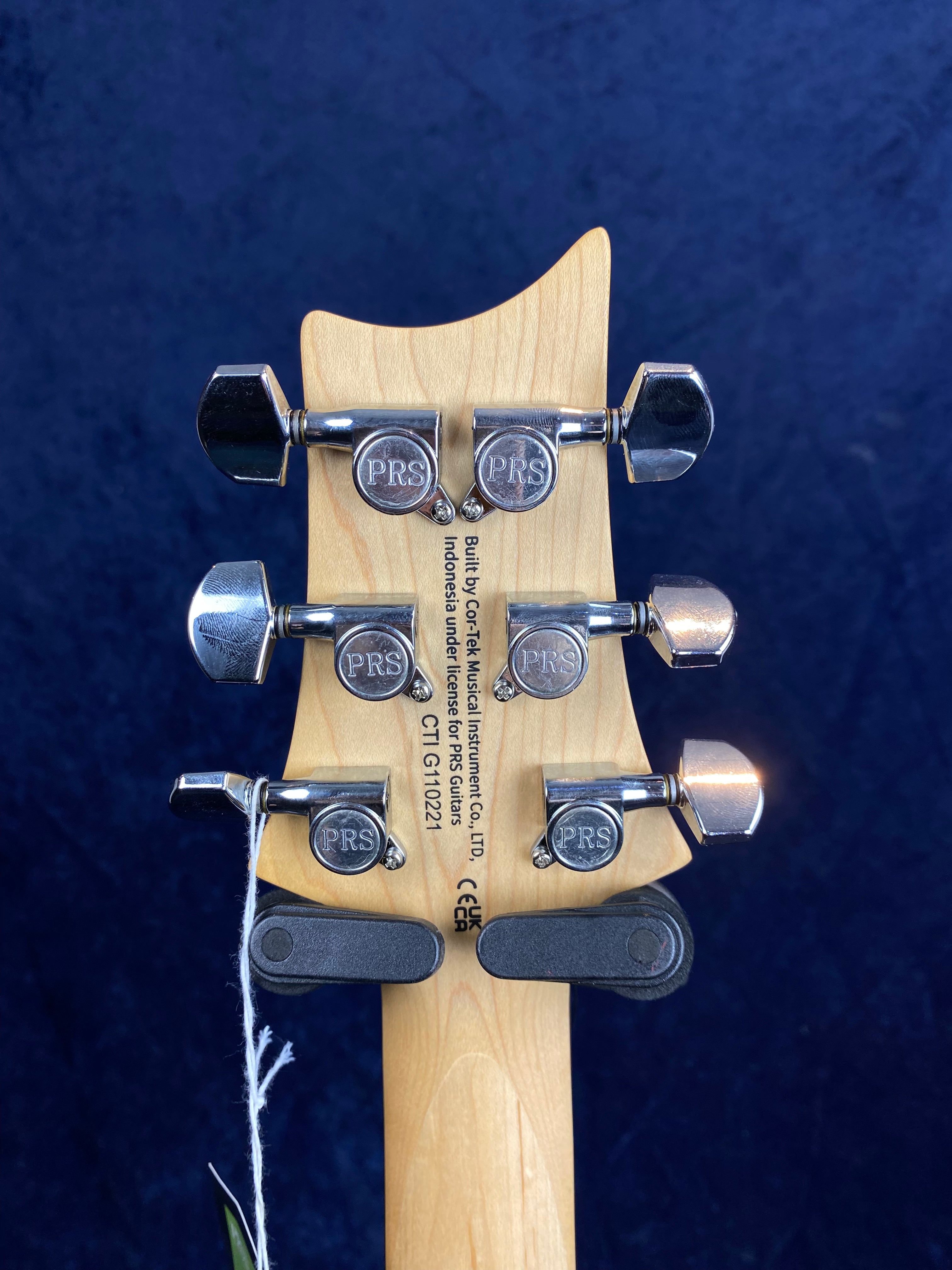 Six chrome tuning pegs labeled PRS are mounted on a light wood electric guitar headstock with black text and a string tied to a lower peg.