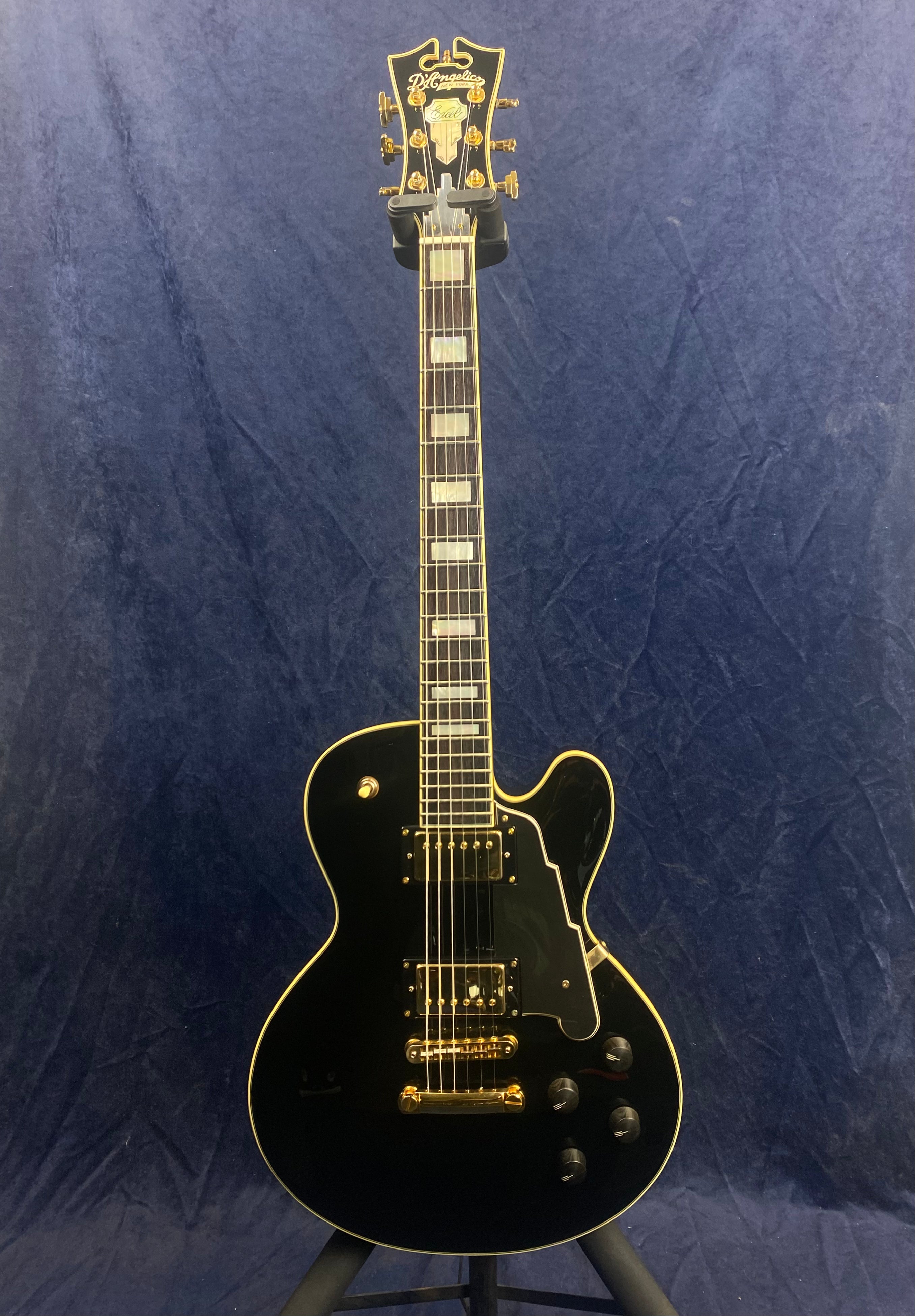 Black electric guitar with gold hardware, rectangular pearl inlays on the fretboard, and a single cutaway body outlined with cream binding.