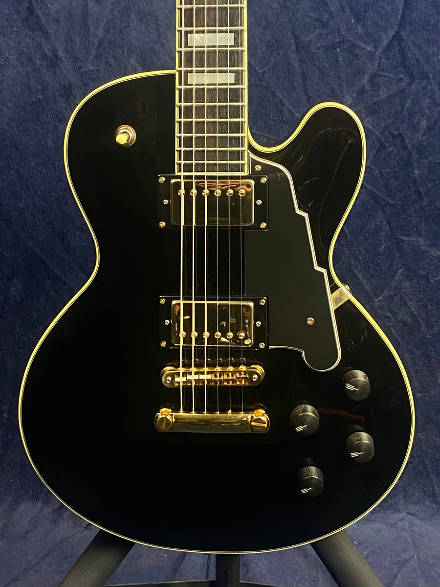 Glossy black electric guitar with gold hardware, cream binding, two humbucker pickups, four black control knobs, and a large angular pickguard.