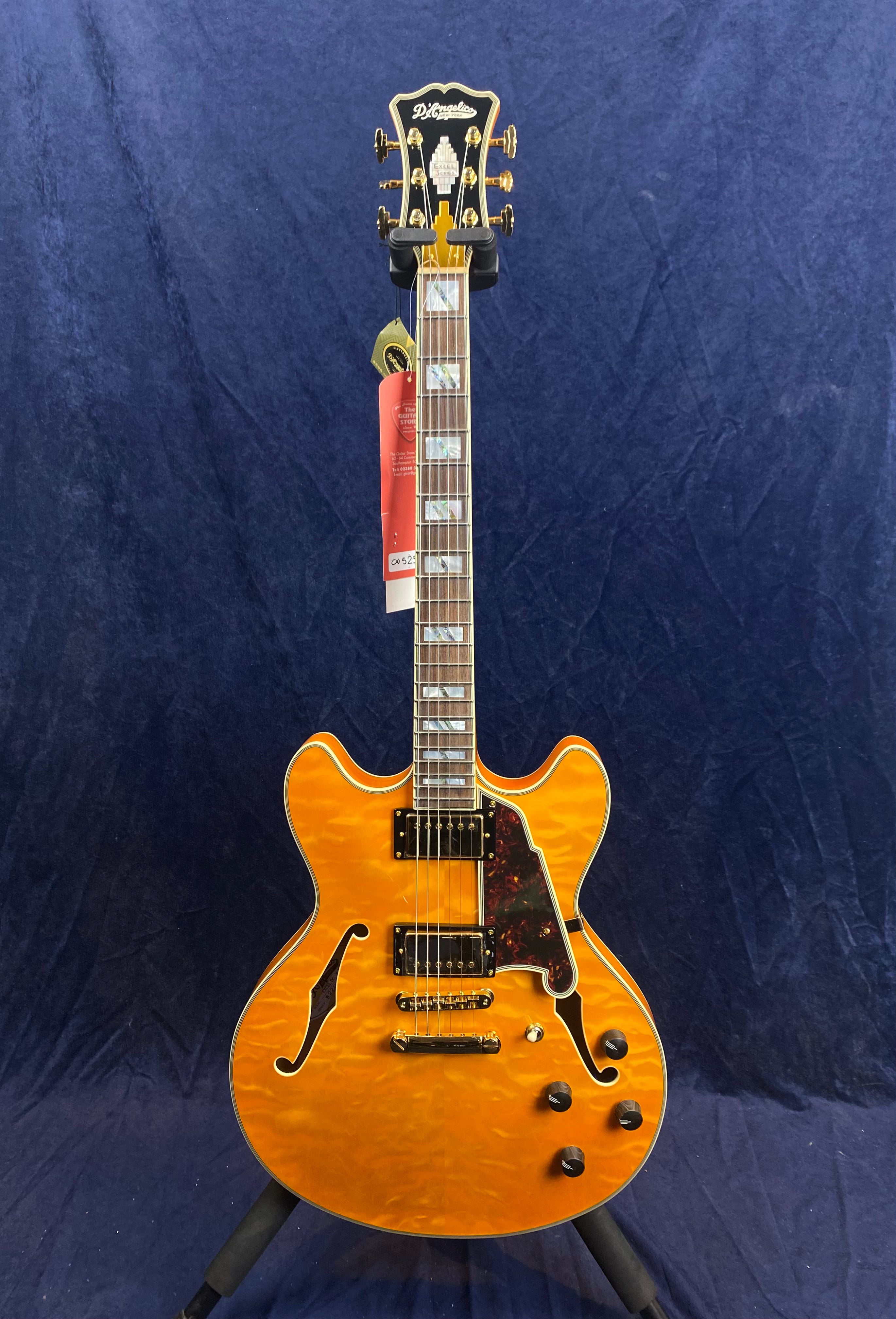 Semi-hollow electric guitar with a quilted amber finish, gold hardware, two humbucker pickups, and f-shaped sound holes, displayed upright on a stand.