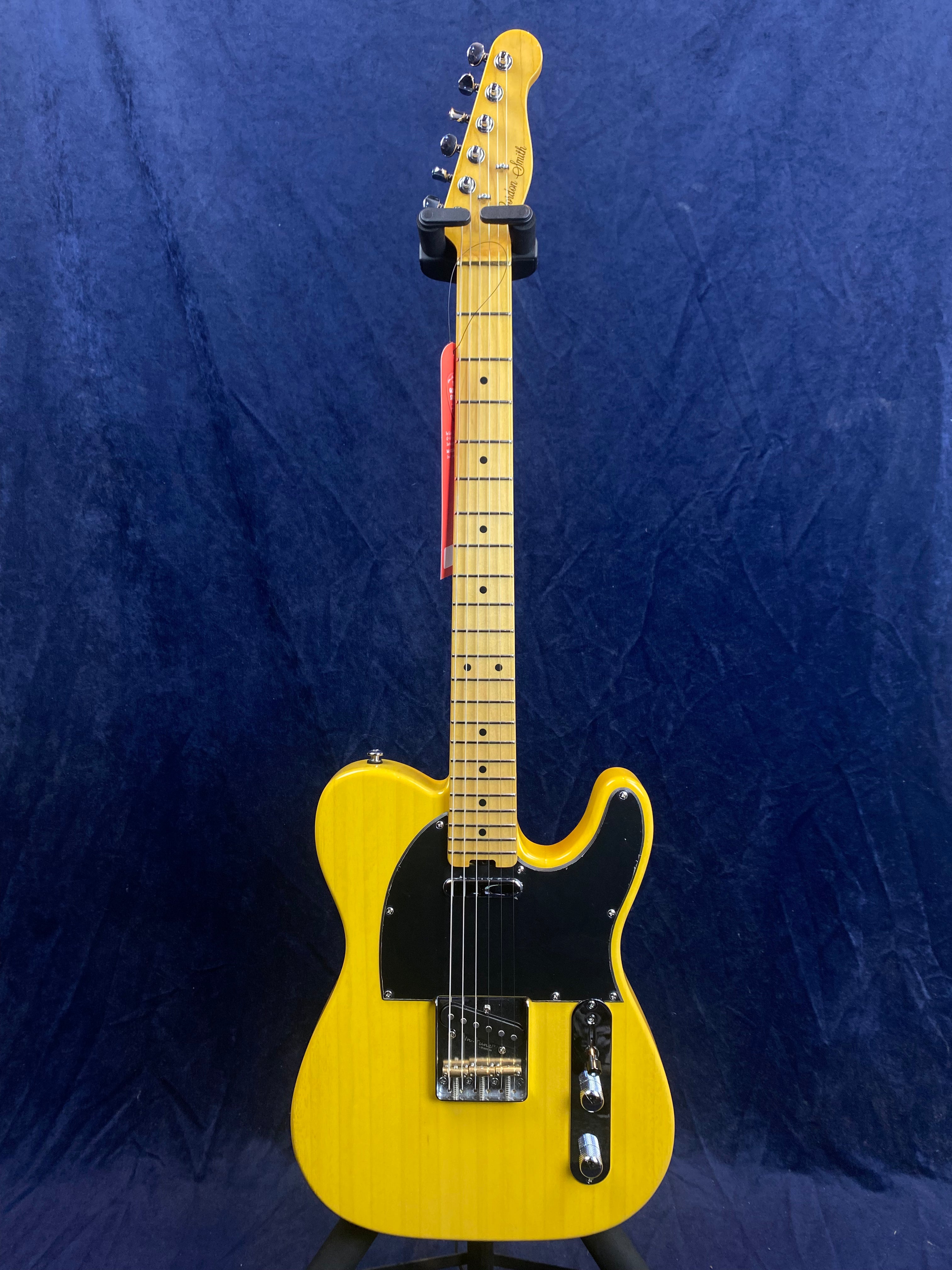 Yellow electric guitar with black pickguard, maple neck, and chrome hardware, displayed upright against a dark blue background.