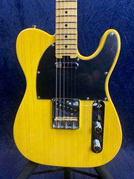 Yellow electric guitar with a black pickguard, chrome bridge, two control knobs, and a maple fretboard, shown against a dark blue background.