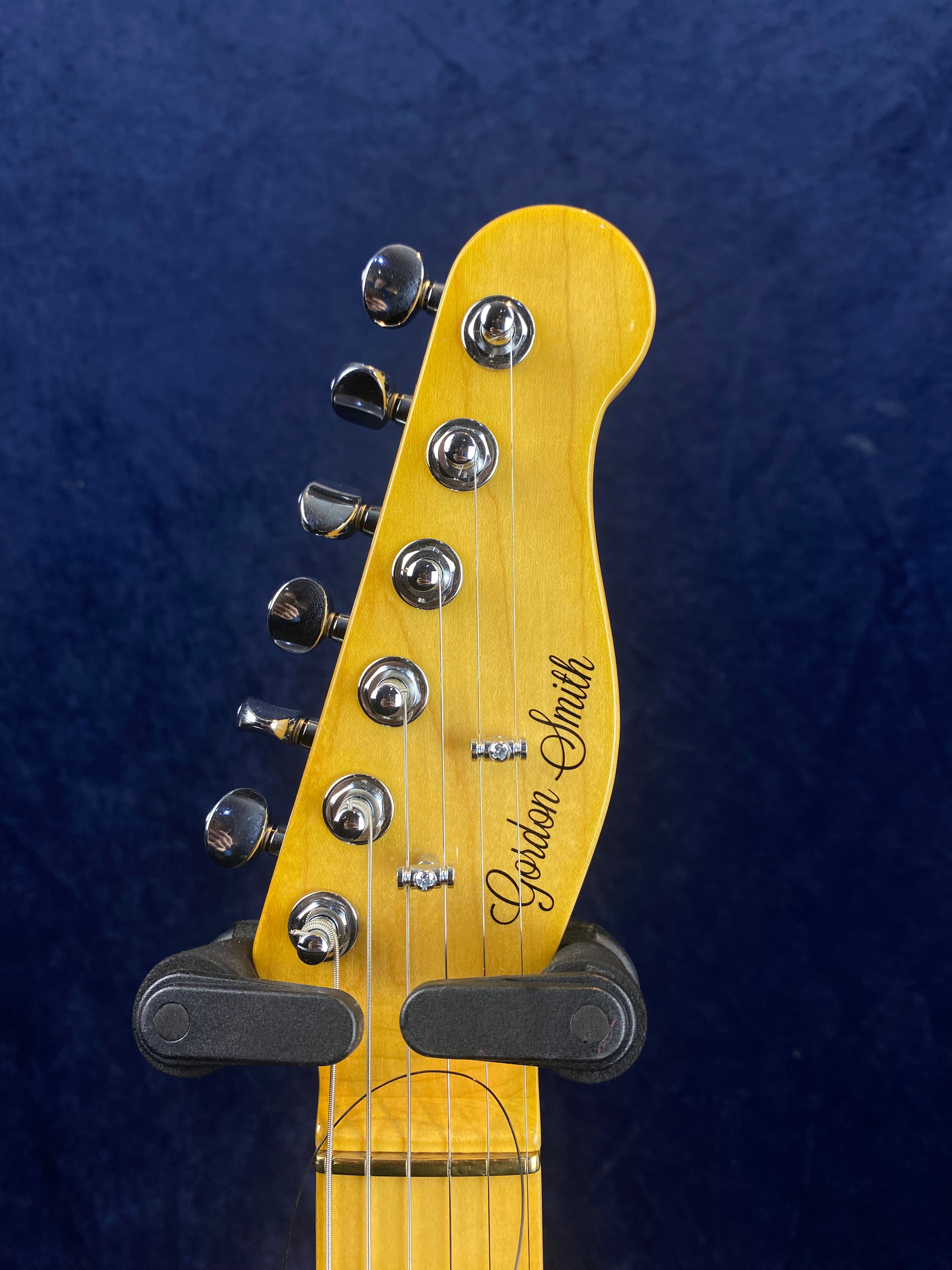 Electric guitar headstock with six chrome tuning pegs, yellow wood finish, and the name "Gordon Smith" in black script.