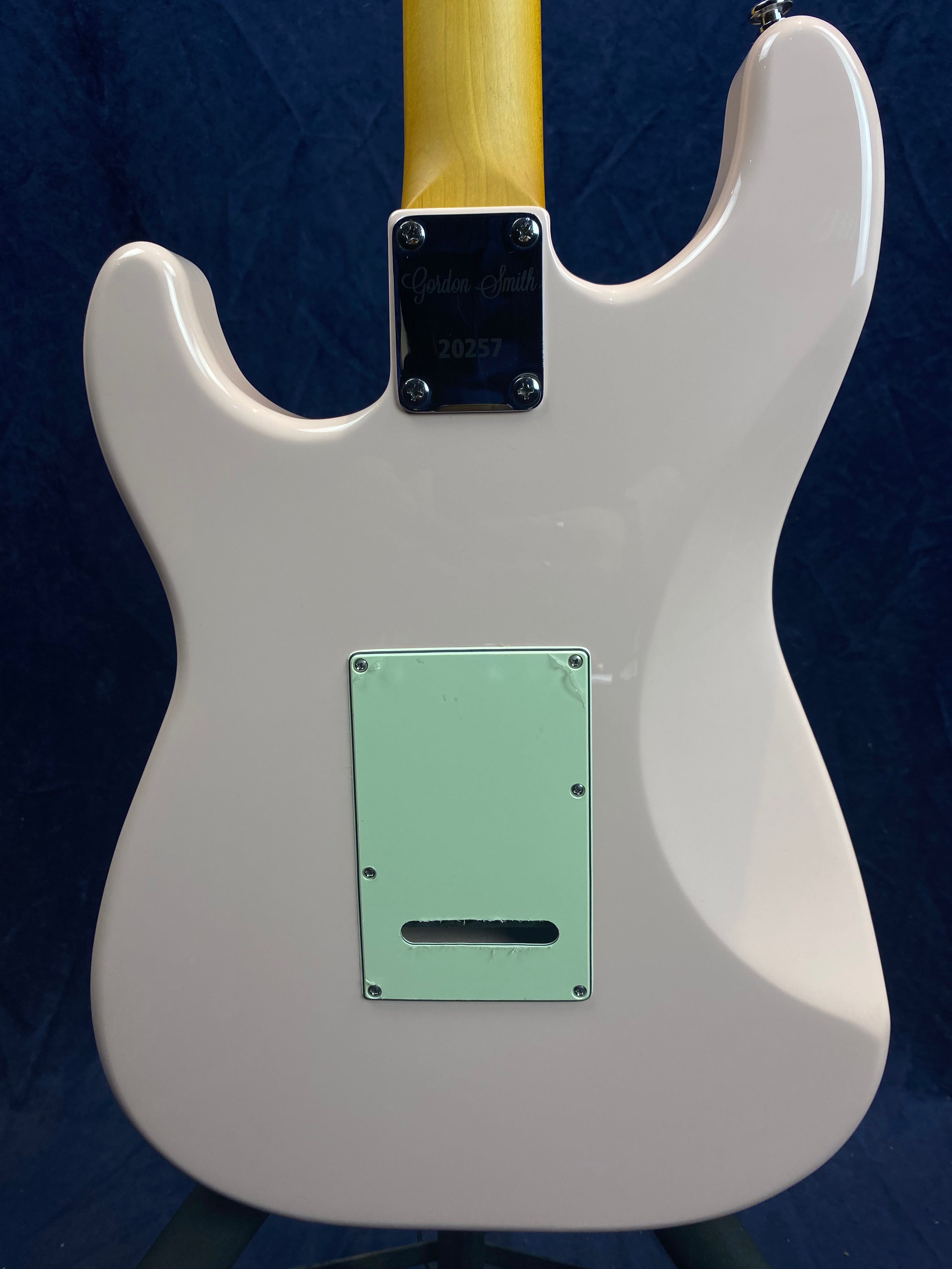 The back of a light pink electric guitar shows a mint green rear cover plate and a neck plate engraved with "Gordon Smith 20257."