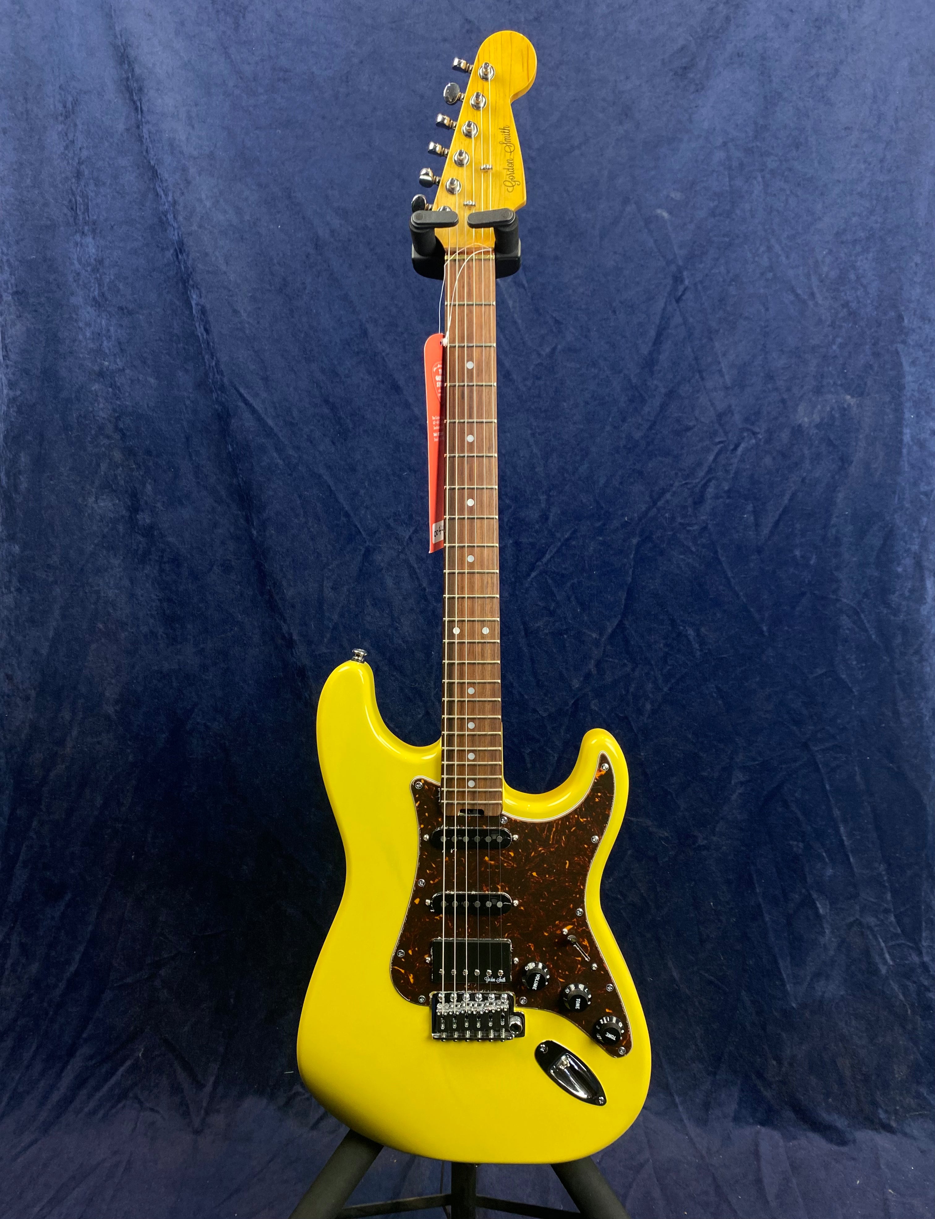 Yellow electric guitar with a dark brown pickguard, six tuning pegs, and a maple neck, displayed upright against a dark blue background.