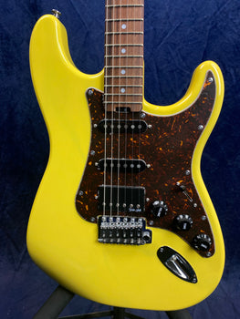 Yellow electric guitar with a brown tortoiseshell pickguard, three pickups, chrome bridge, and black control knobs against a dark blue background.