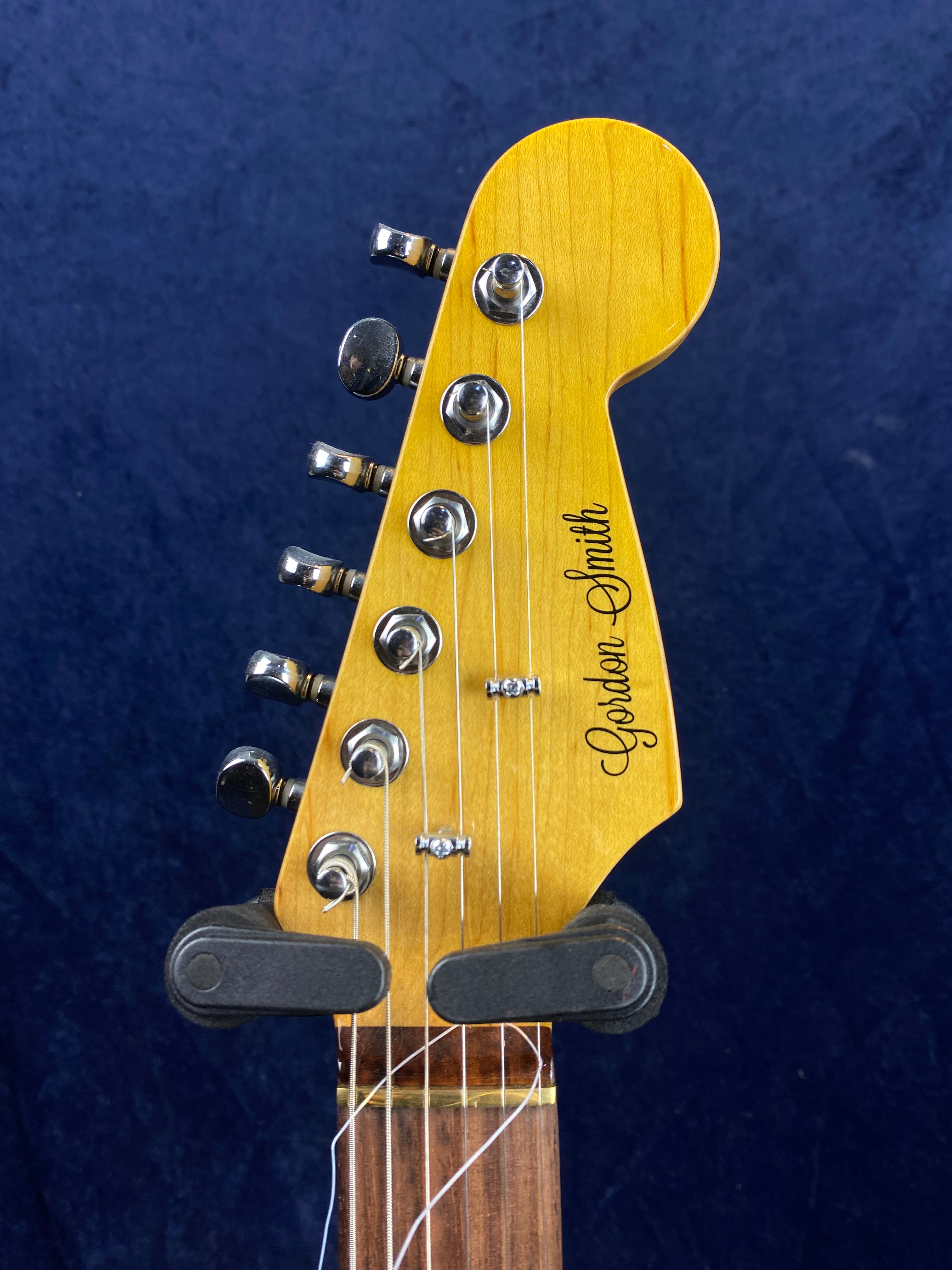 Electric guitar headstock with six tuning pegs and "Gordon Smith" written in black script on the light wood.