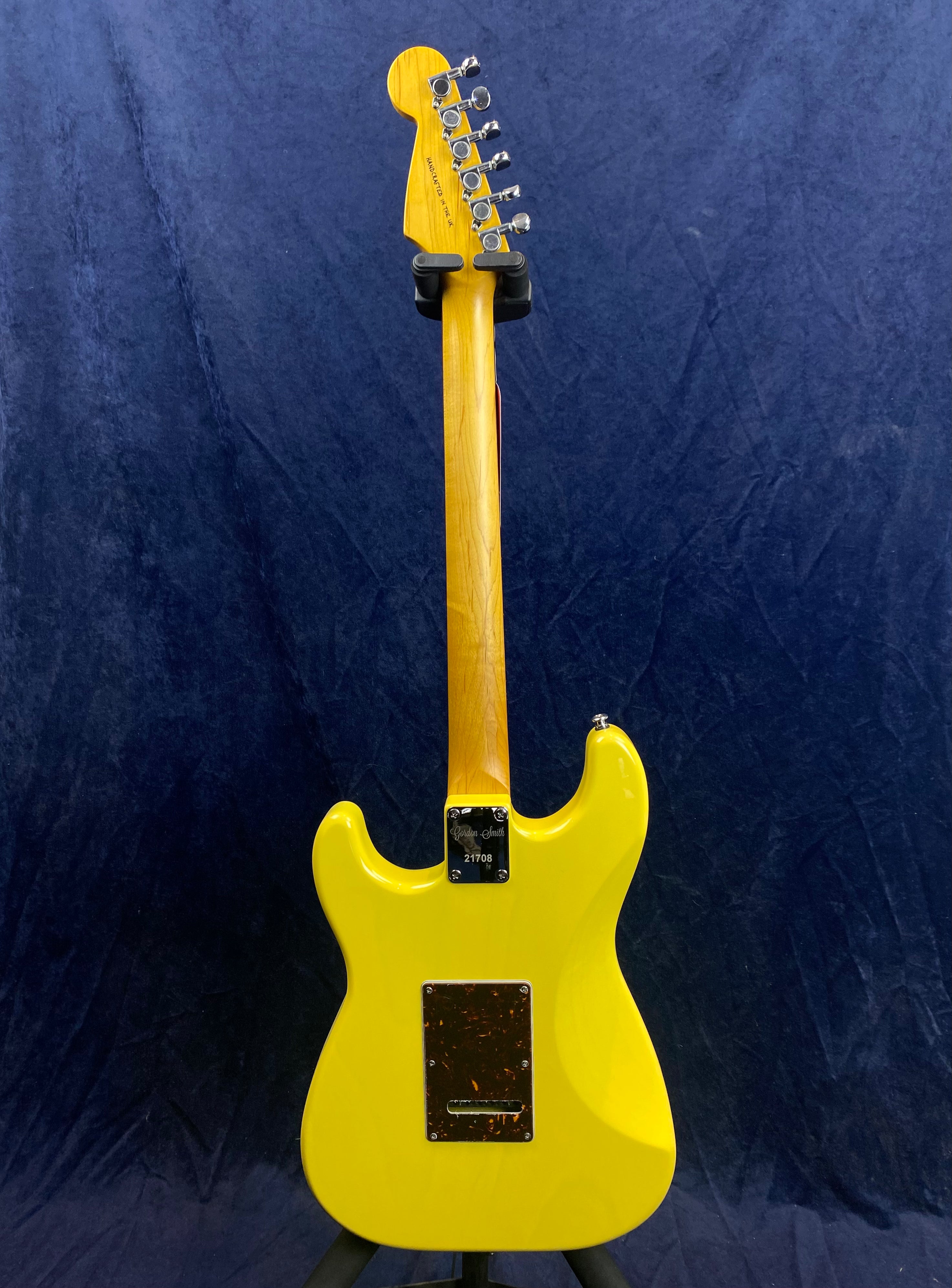 Yellow electric guitar shown from the back, featuring a natural wood neck, six tuning pegs, and a rectangular rear electronics cover plate.