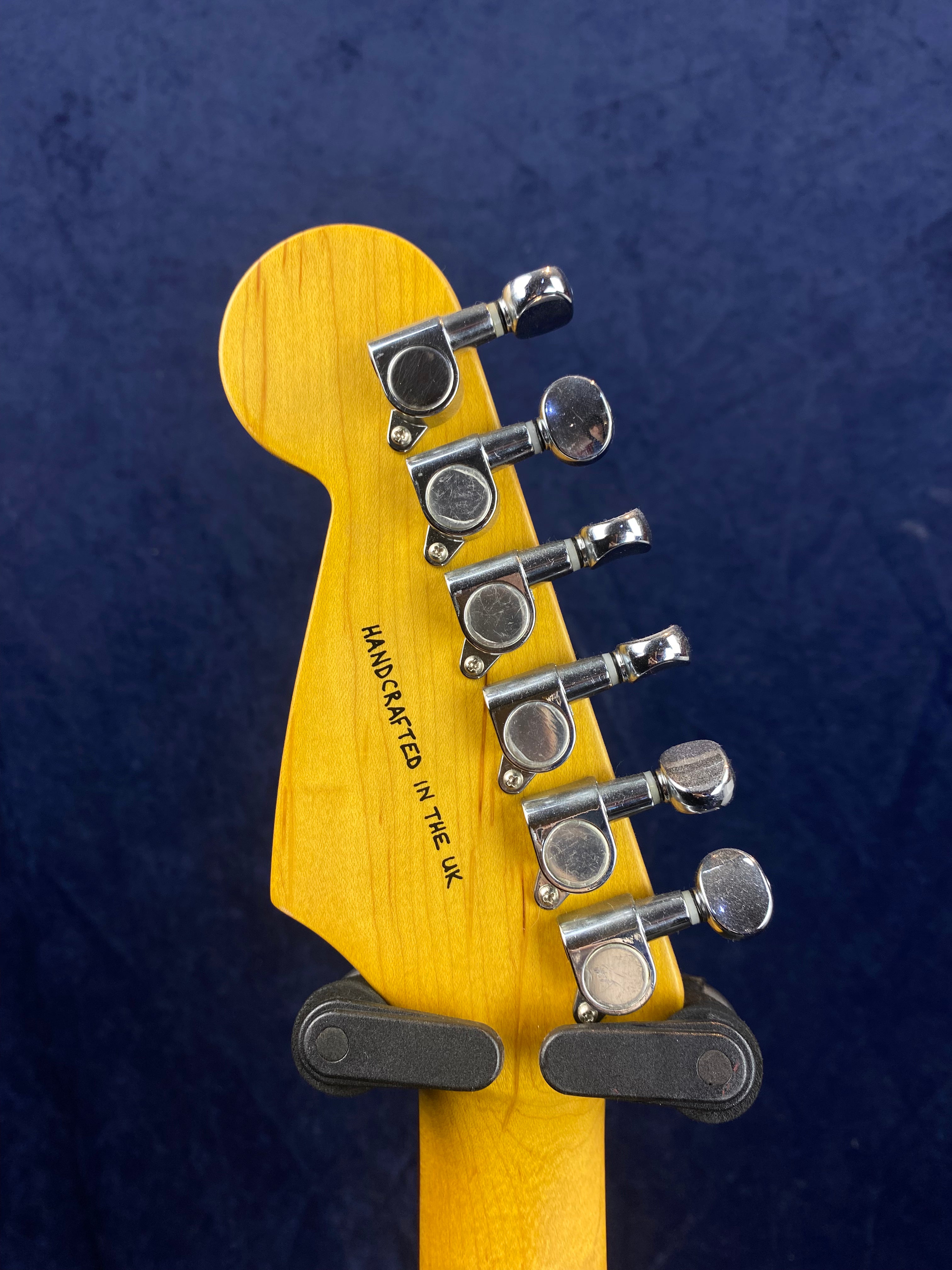 Electric guitar headstock with six chrome tuning pegs, yellow wood finish, and "Handcrafted in the UK" text on the back.