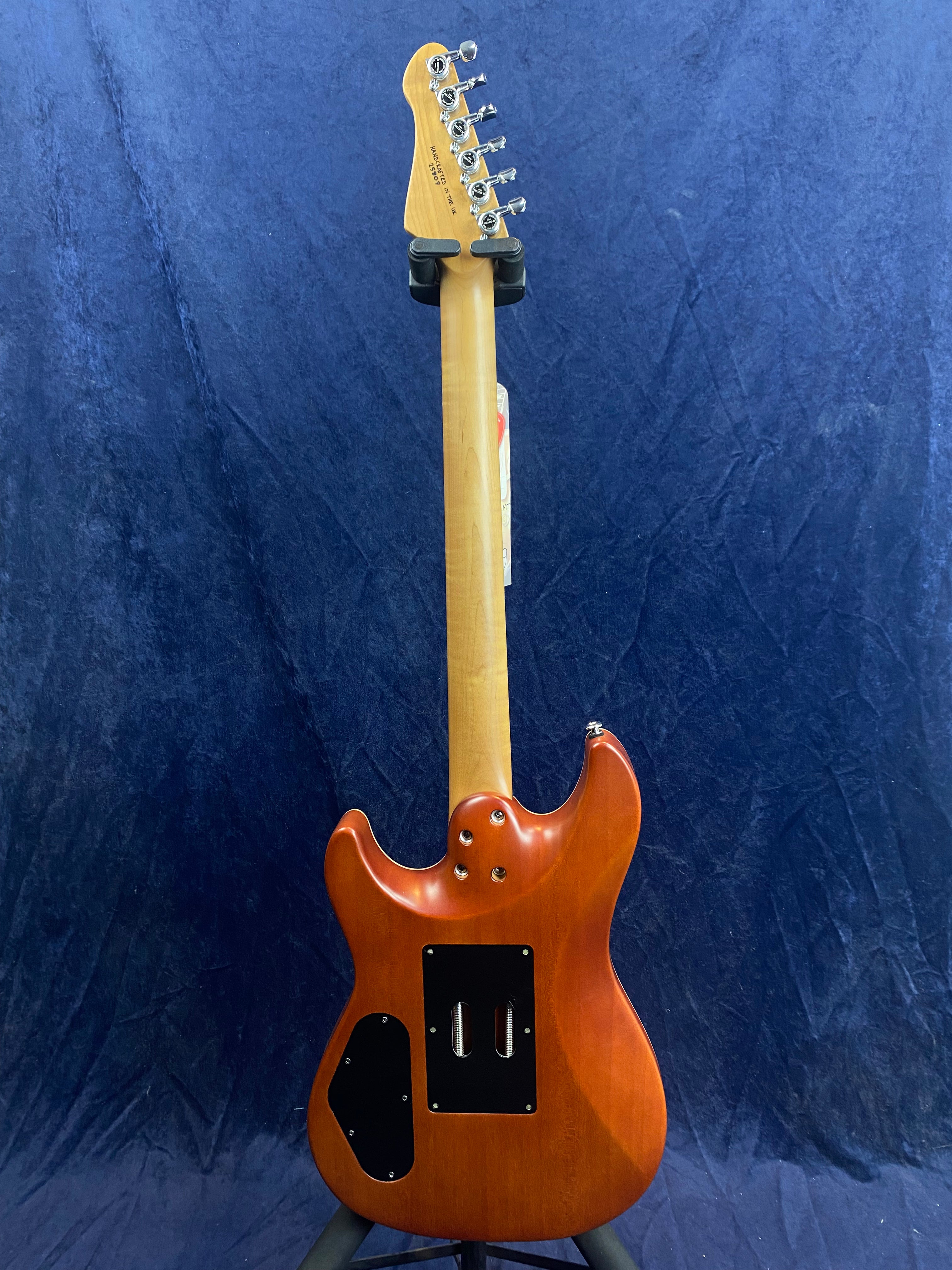 Electric guitar shown from the back, natural wood neck and reddish-brown body with two black plastic cavity covers, standing against a blue background.