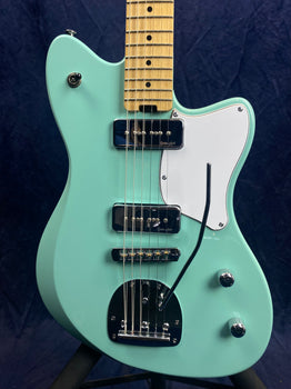 Mint green electric guitar with chrome hardware, two black pickups, white pickguard, maple neck, three control knobs, and a tremolo arm.