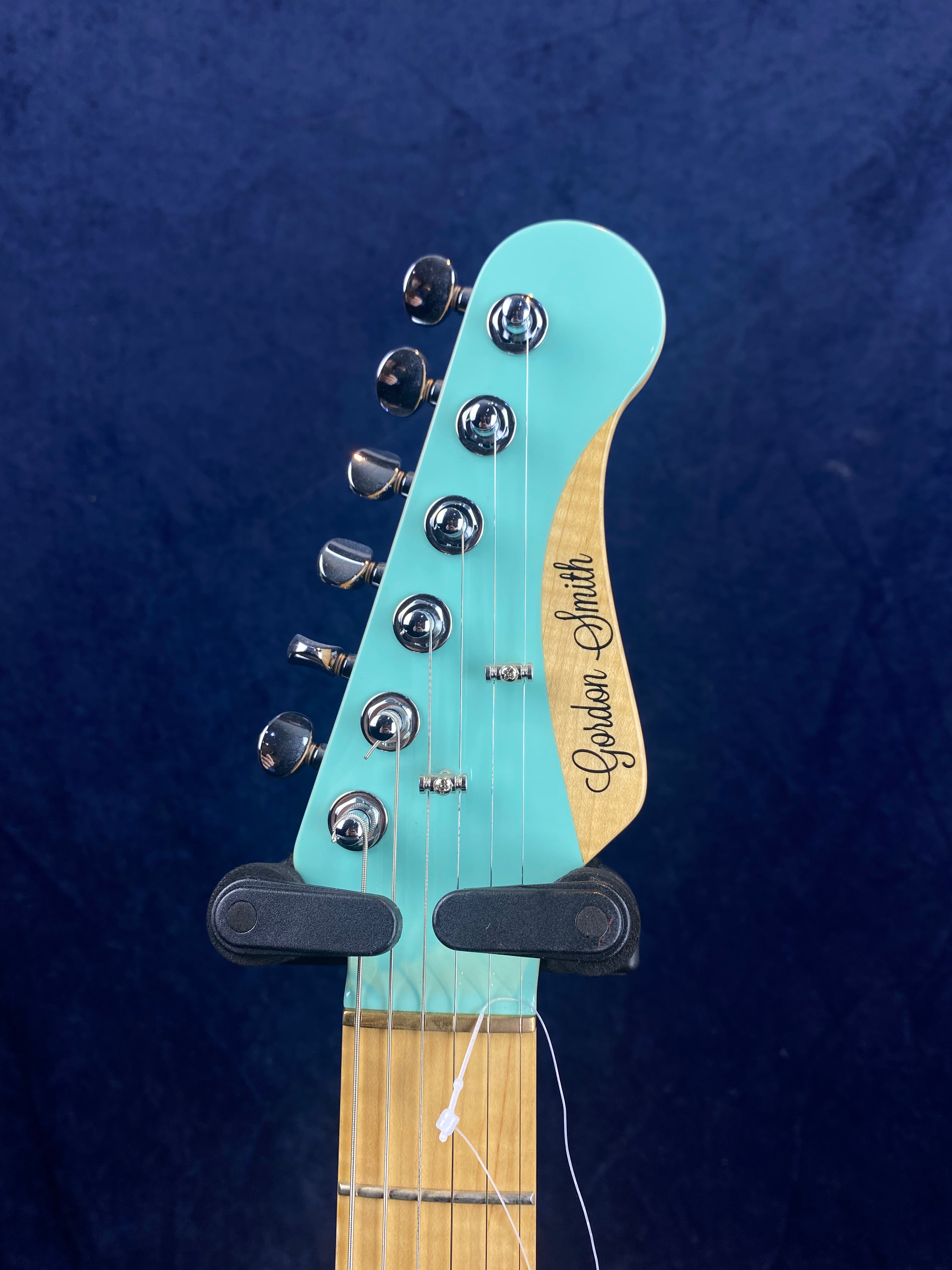Electric guitar headstock in light blue with six chrome tuning pegs, maple wood accent, and "Gordon Smith" logo in script.