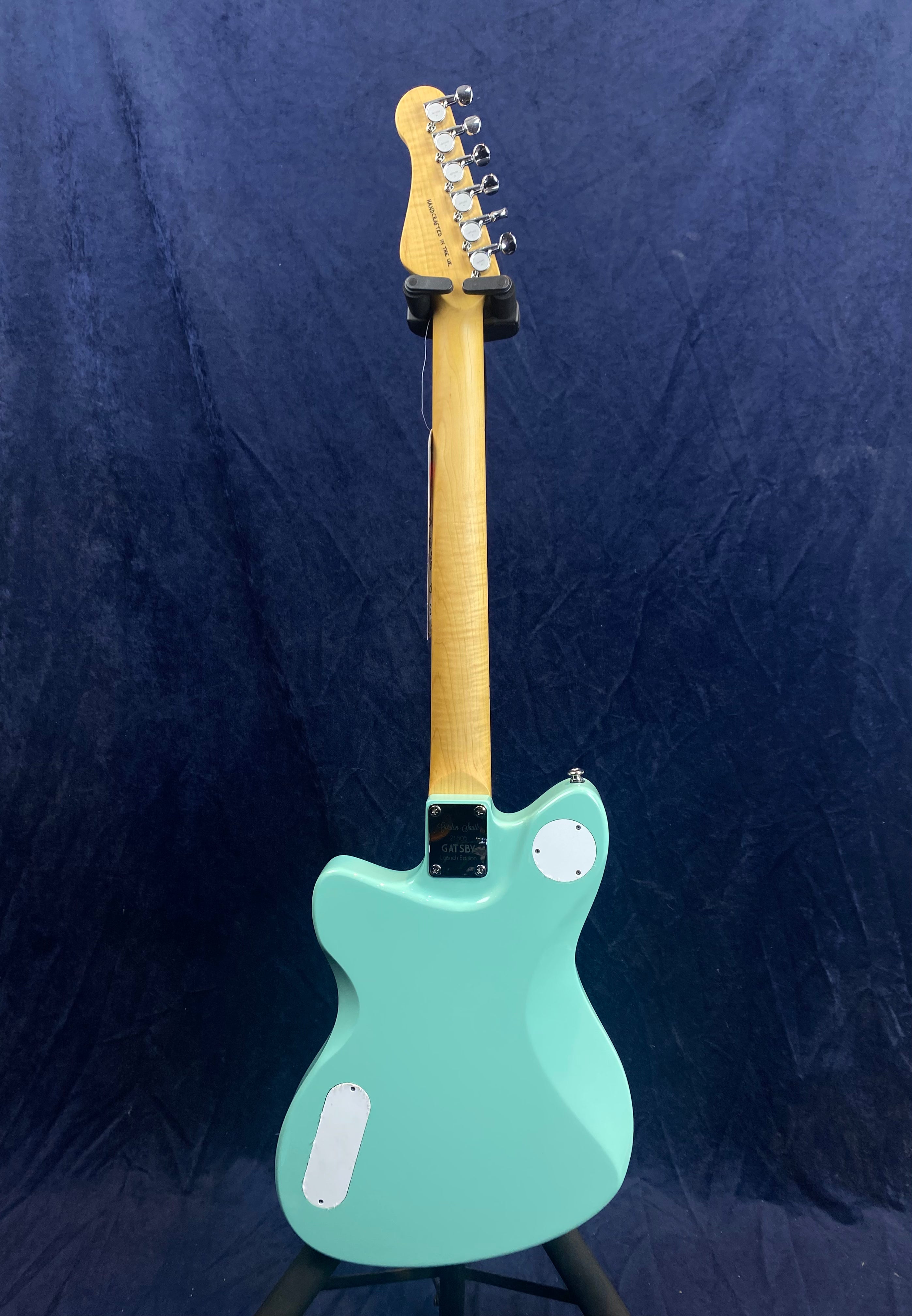 A mint green electric guitar viewed from the back, showing a light wood neck, metal tuning pegs, and two white back panels for electronics.