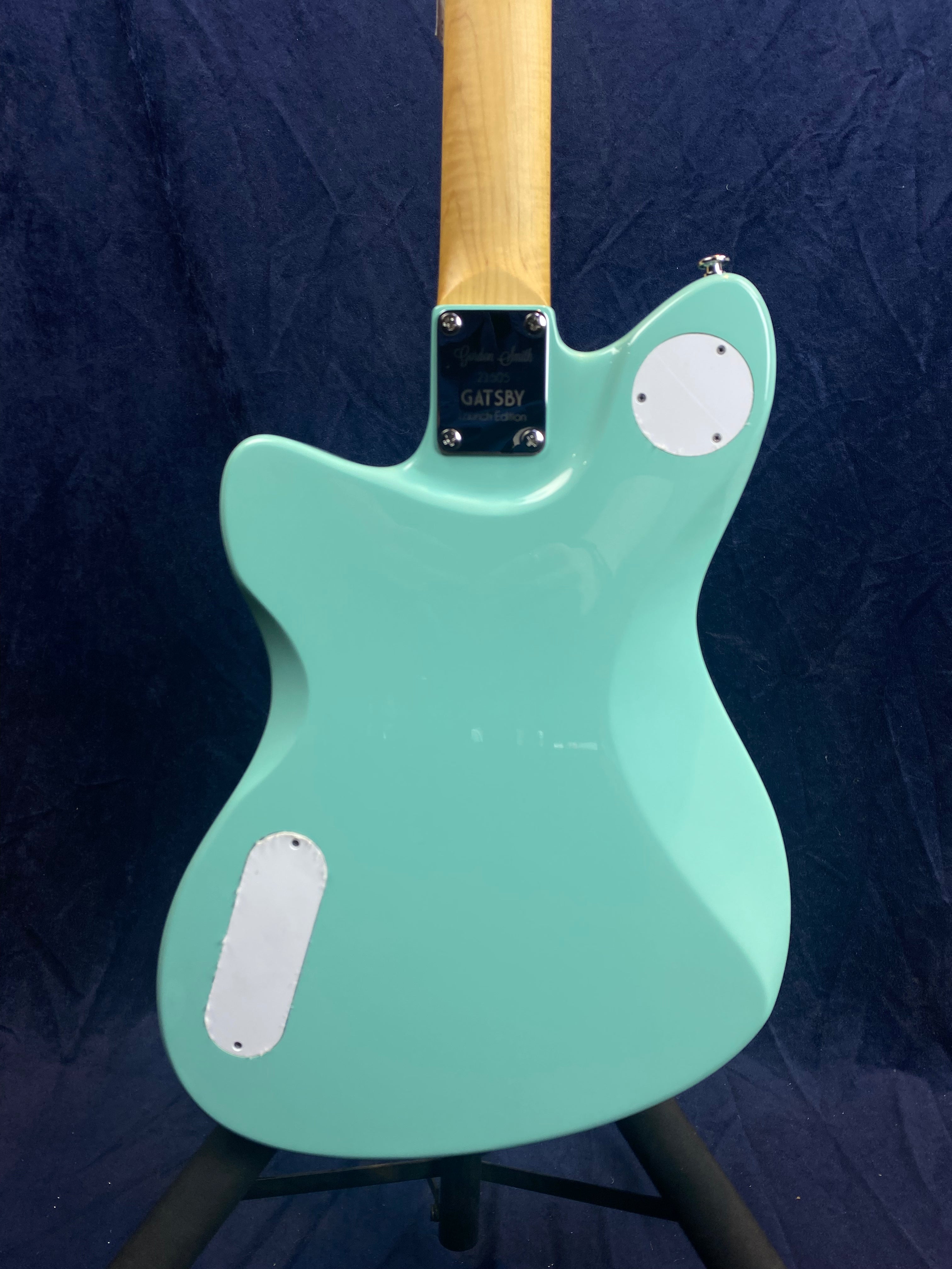 Mint green electric guitar back, with a natural wood neck and two white plastic cover plates on the body.