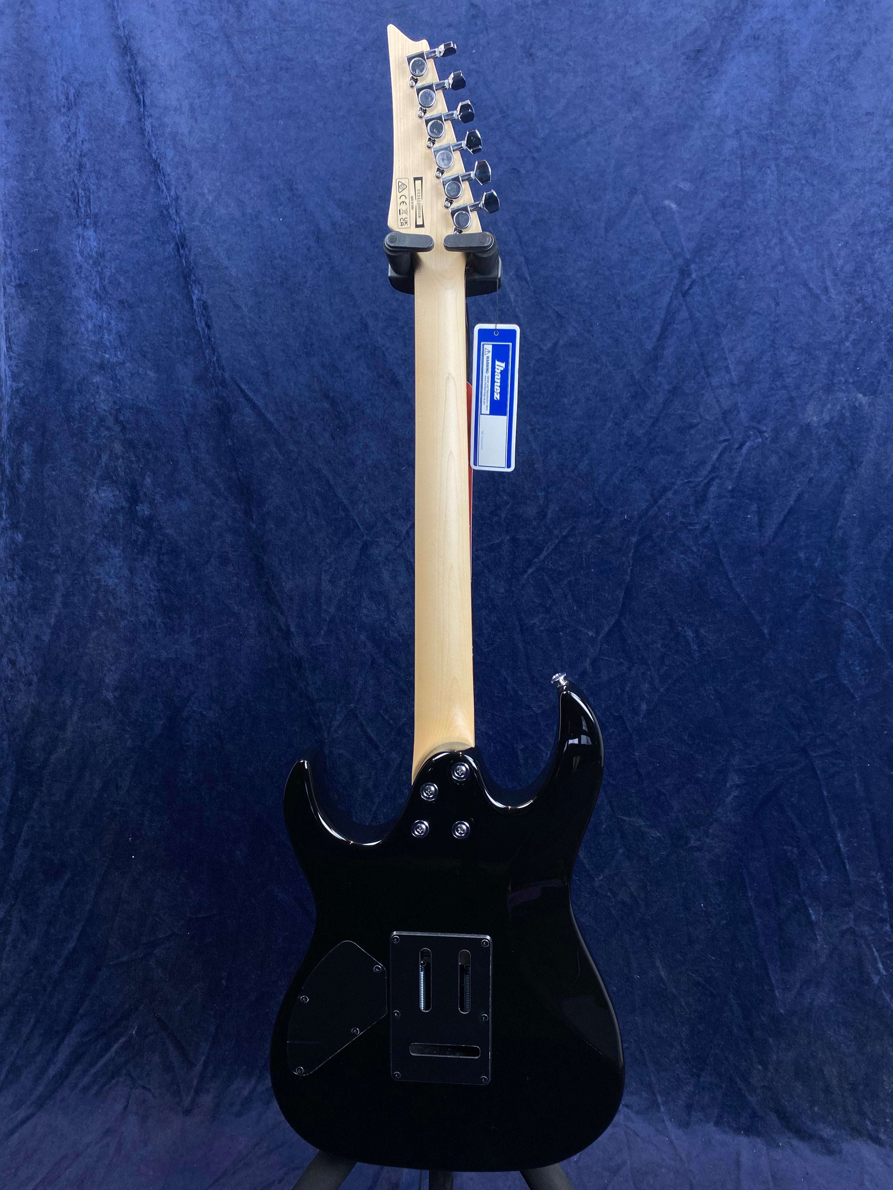 Black electric guitar shown from the back, with a light wood neck, chrome tuning pegs, and an Ibanez tag hanging from the headstock.