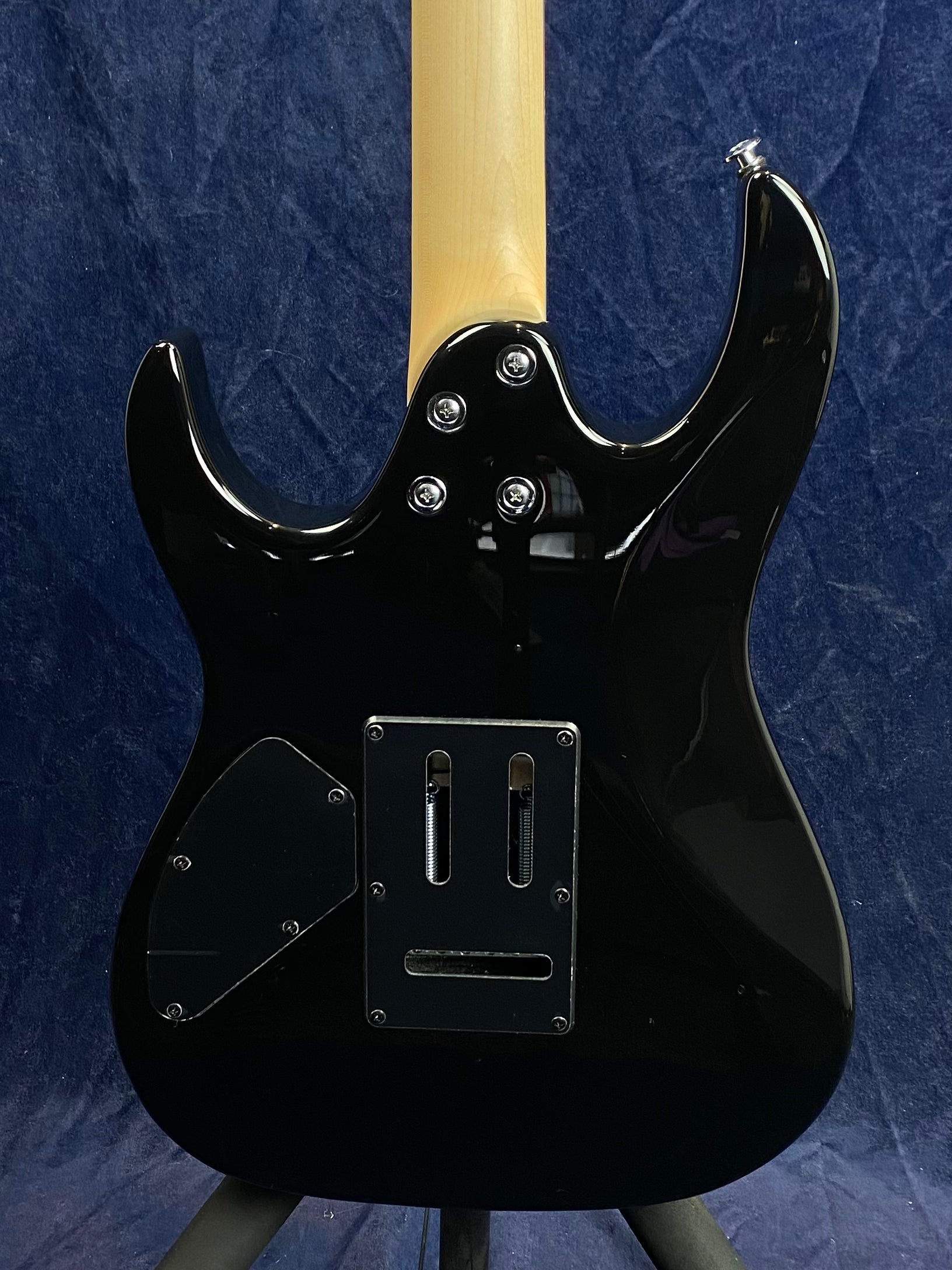 Black electric guitar shown from the back, natural wood neck, metal bolt attachments, two rear access panels, and exposed tremolo spring cavity.