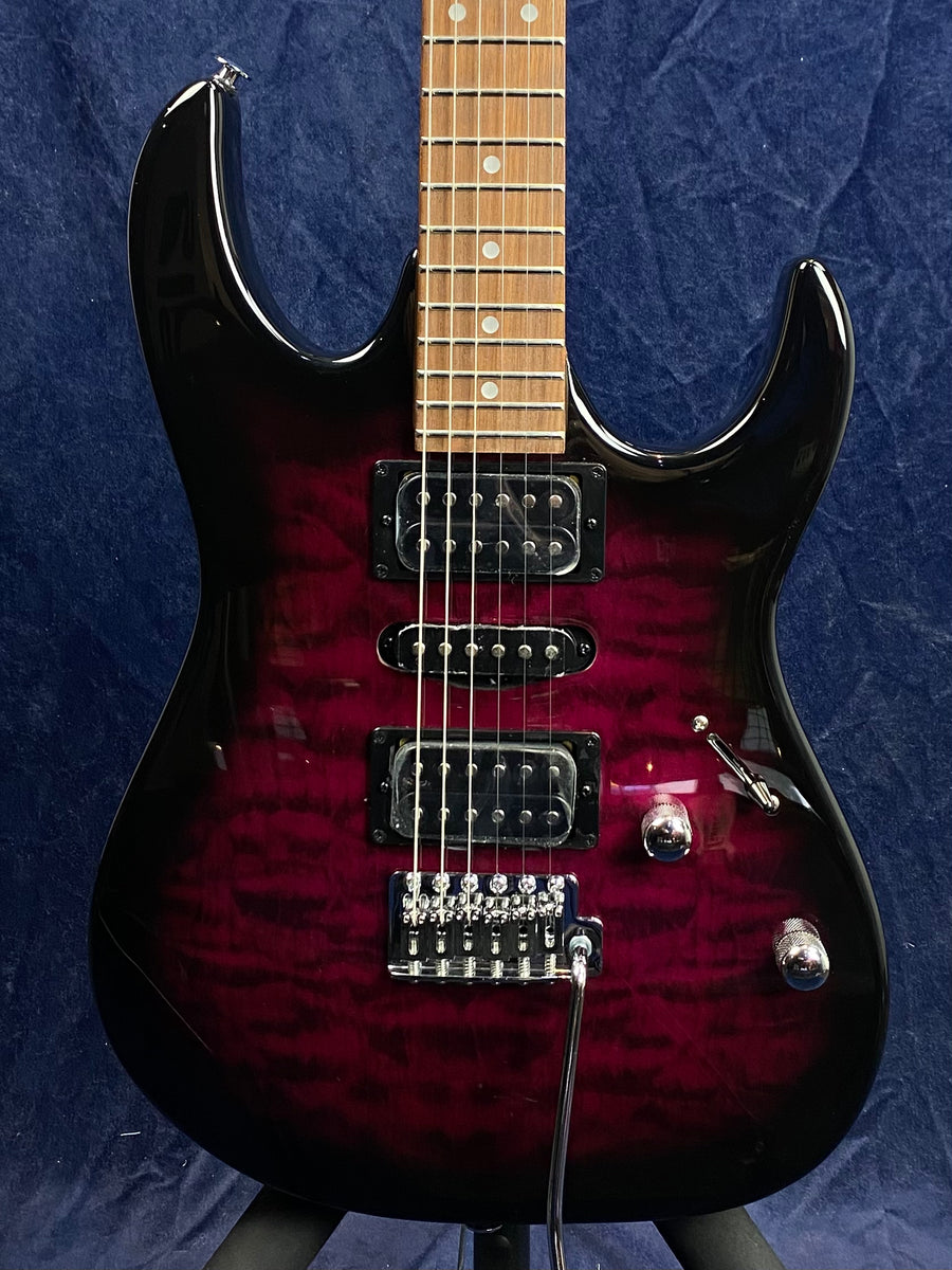 Electric guitar with a deep red and black finish, two humbucker pickups, one single coil pickup, a tremolo bridge, and two control knobs.