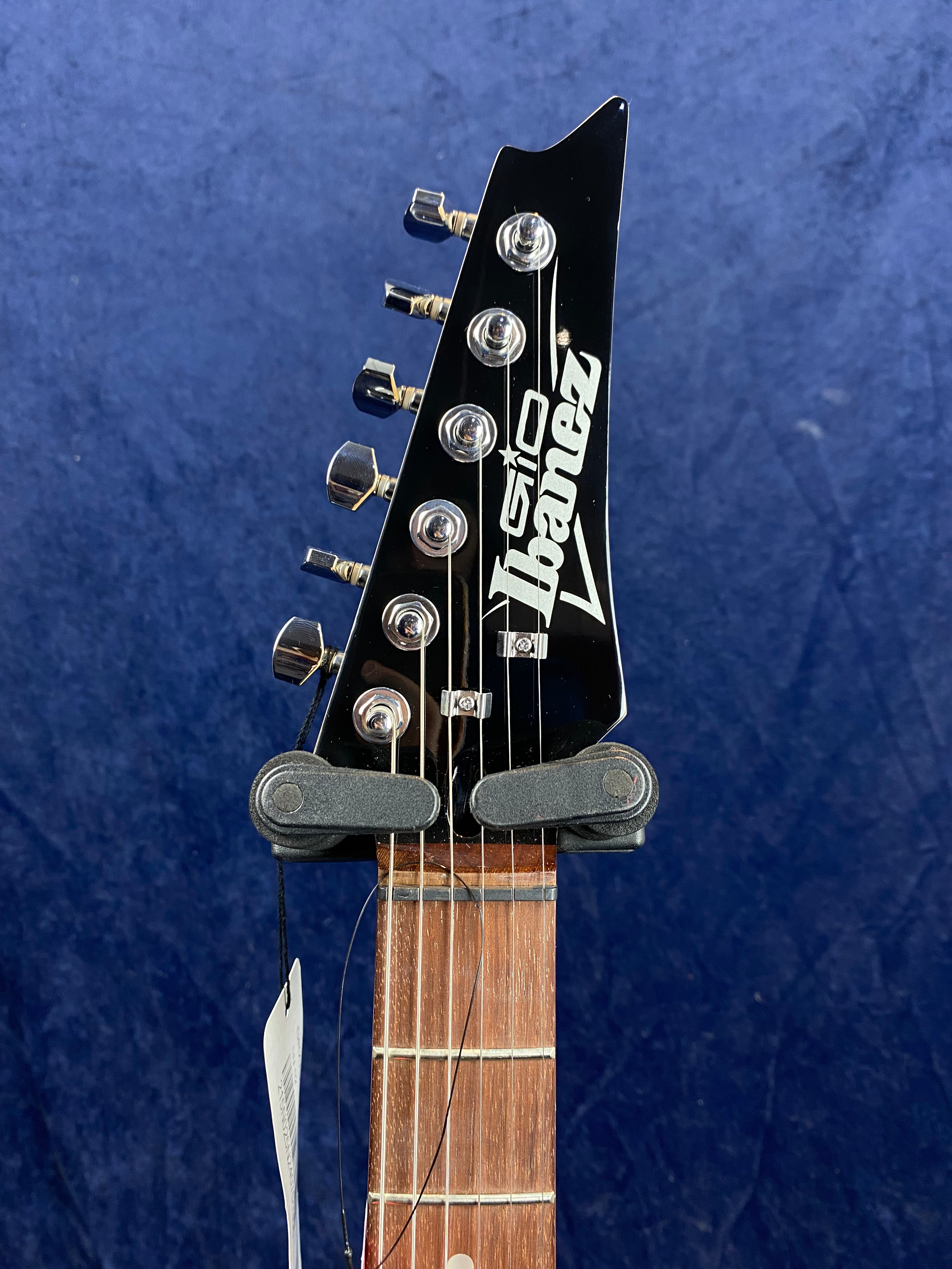 Ibanez electric guitar headstock with six chrome tuning pegs on a black background, white logo, and part of rosewood fretboard visible.