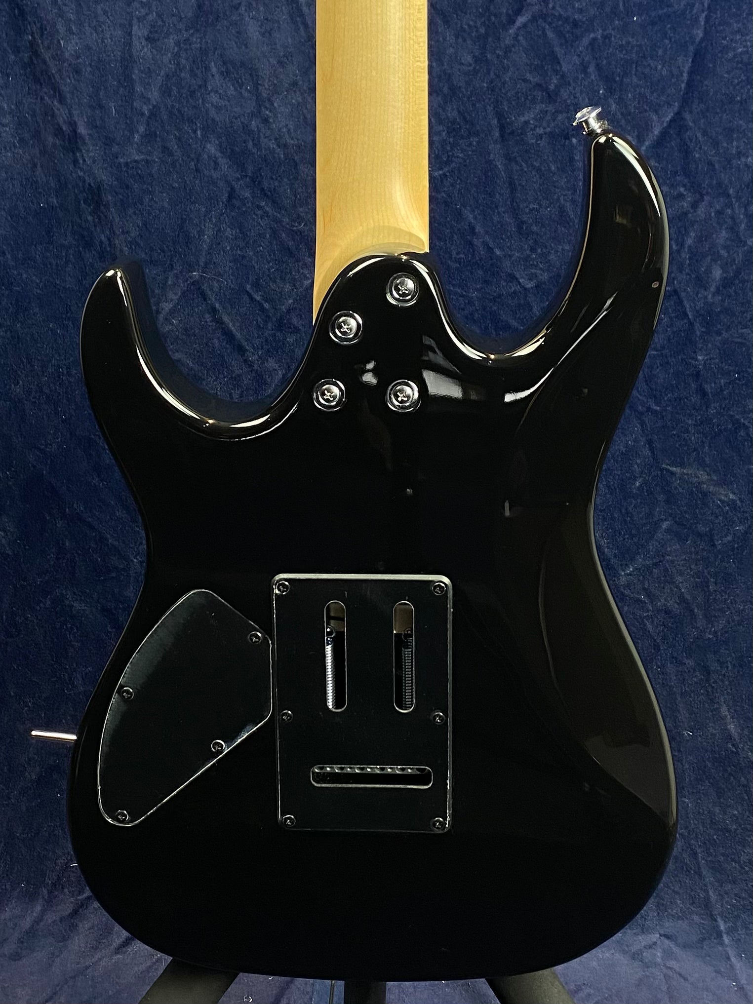 Black electric guitar back view showing bolt-on neck with four screws, rear control cavity covers, and exposed tremolo spring cavity.