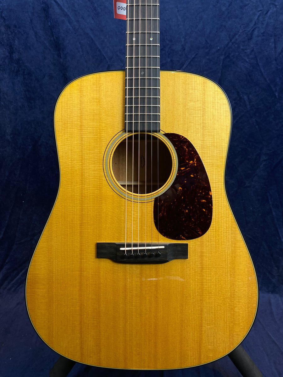Acoustic guitar with a light wood body, black bridge, dark tortoiseshell pickguard, round sound hole, and dot inlays on a dark fretboard.