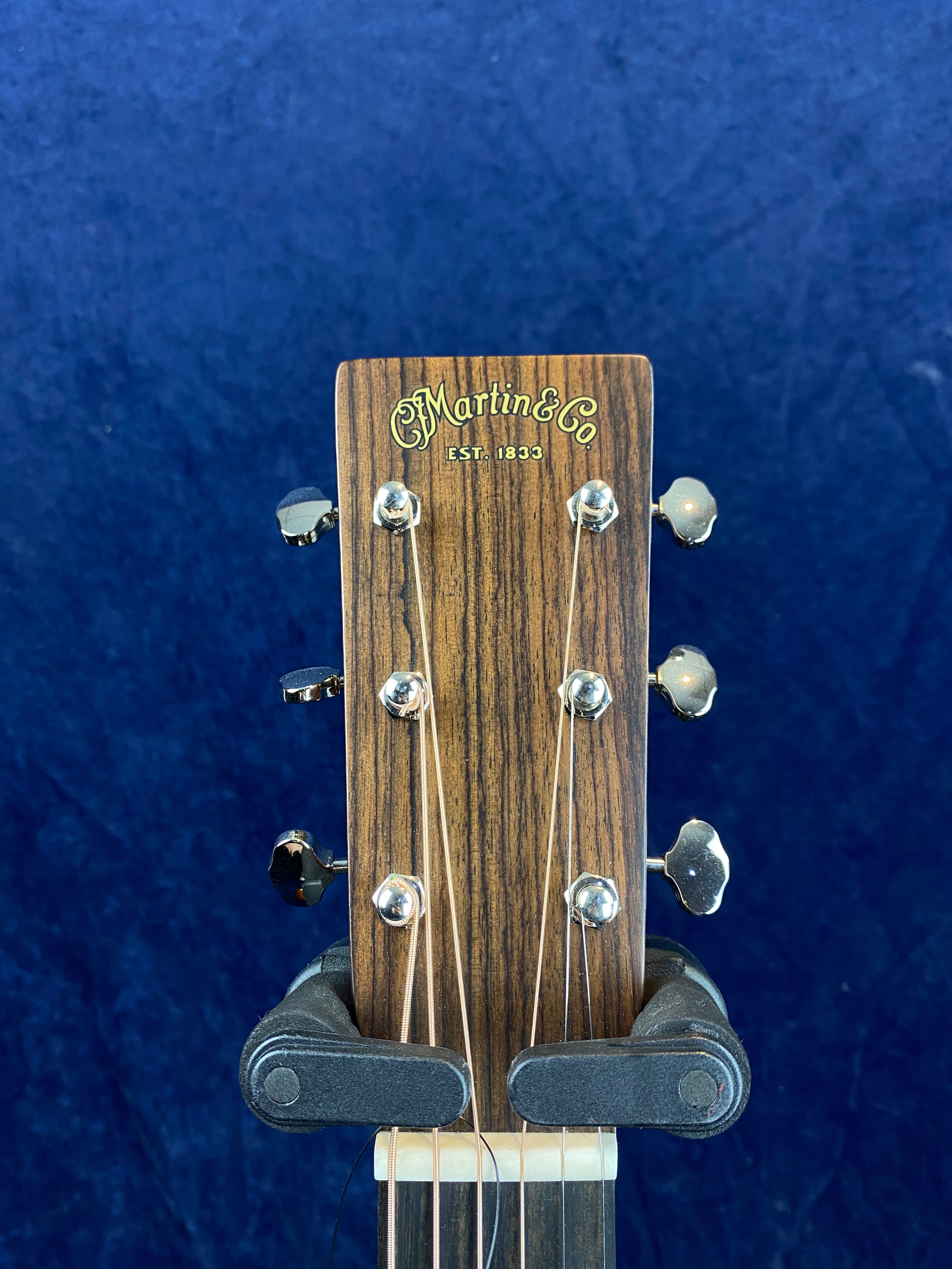 The headstock of a Martin & Co acoustic guitar with six tuning pegs, displayed against a dark blue background.