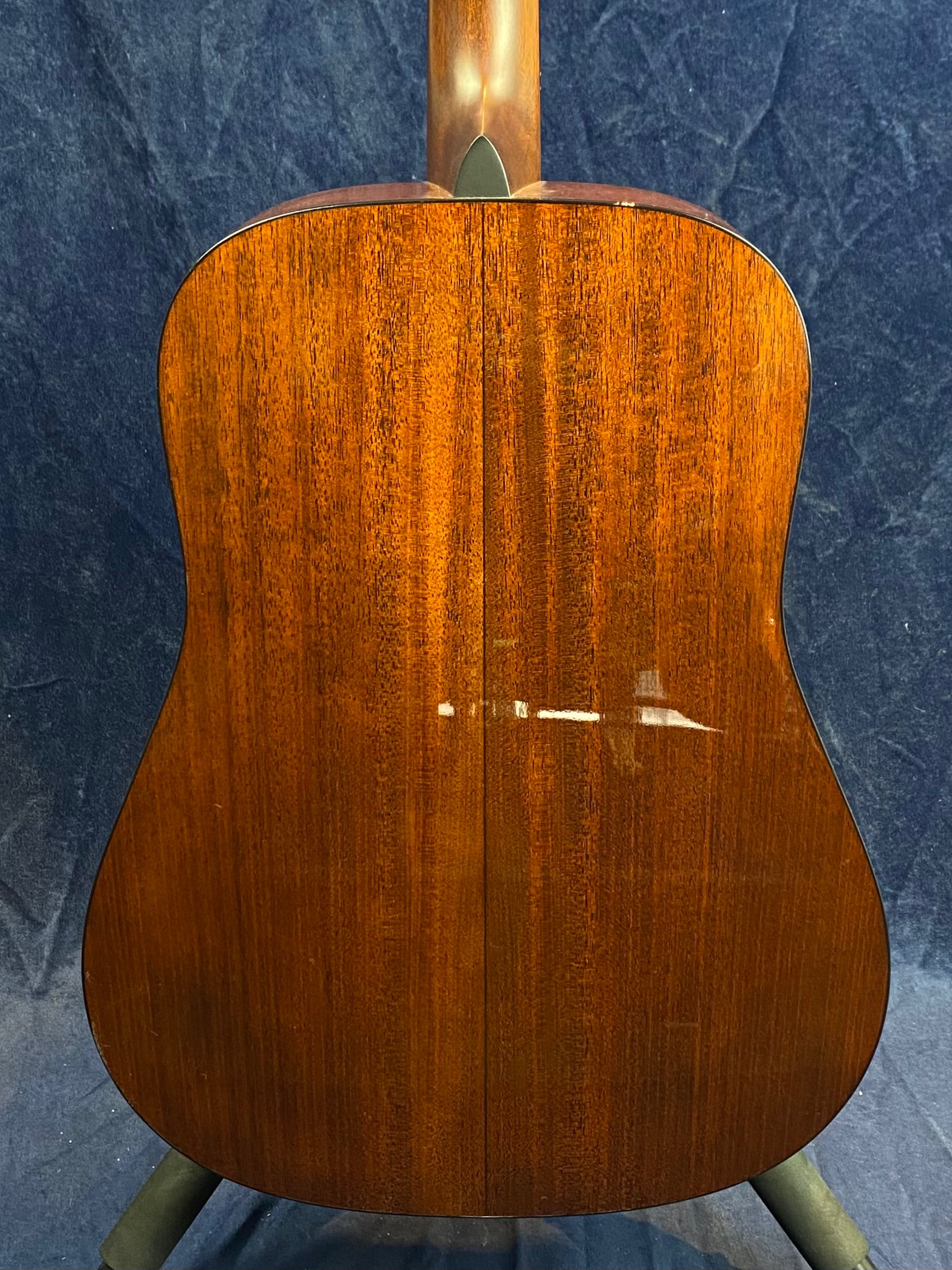Rich brown acoustic guitar back with a glossy wood finish, showing a vertical seam down the center and gentle wood grain patterns.