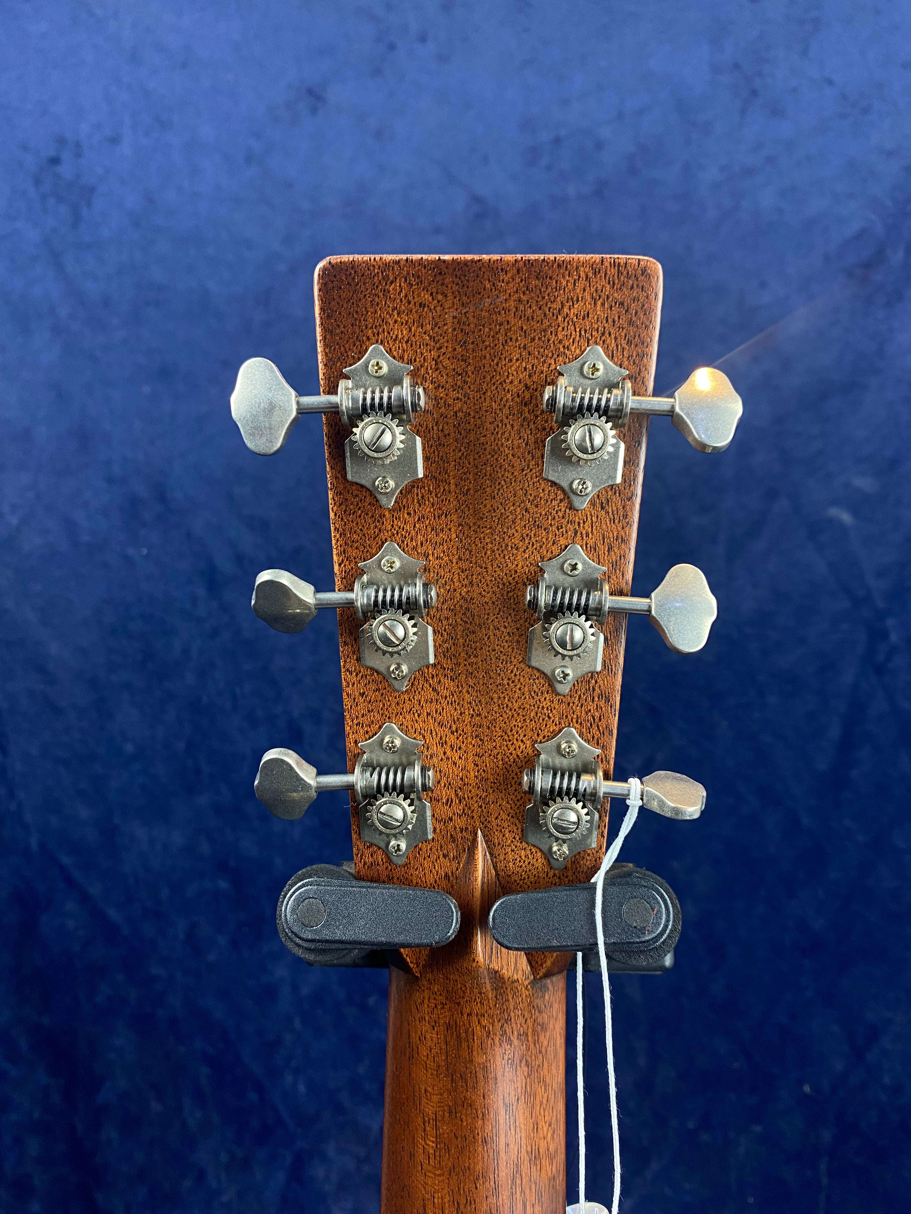 Six metal tuning pegs attached to the back of a wooden acoustic guitar headstock, shown against a solid blue background.
