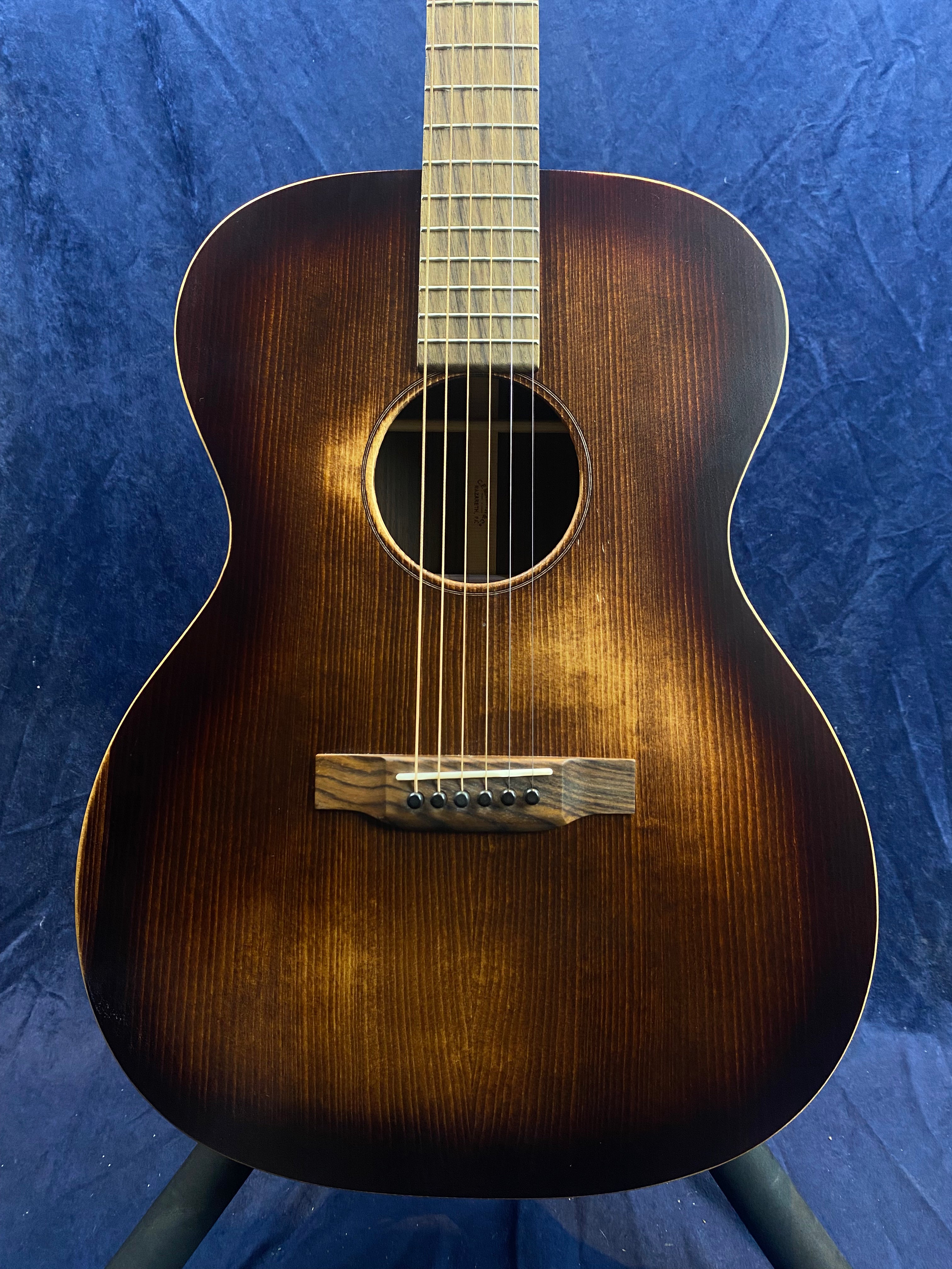 Small-bodied acoustic guitar with a dark sunburst finish, six strings, light-colored wooden bridge, and cream binding around the top edge.